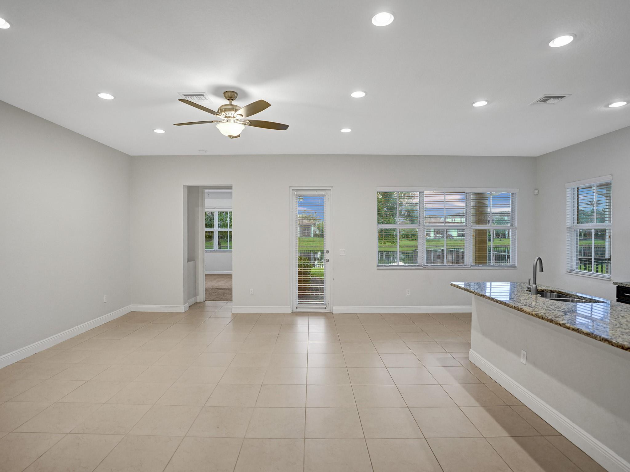 Vacant kitchen and dining area with tiled floors, granite peninsula, and windows overlooking a fenced lawn.