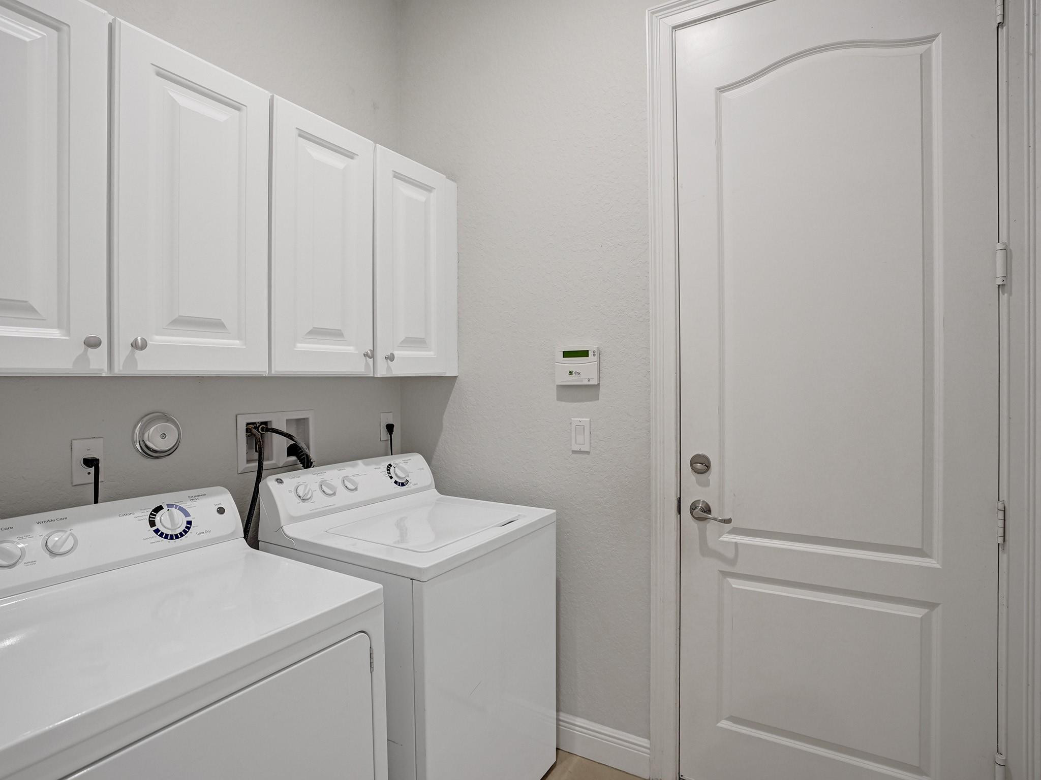 Laundry room with white washer and dryer beneath wall cabinets beside a paneled door.