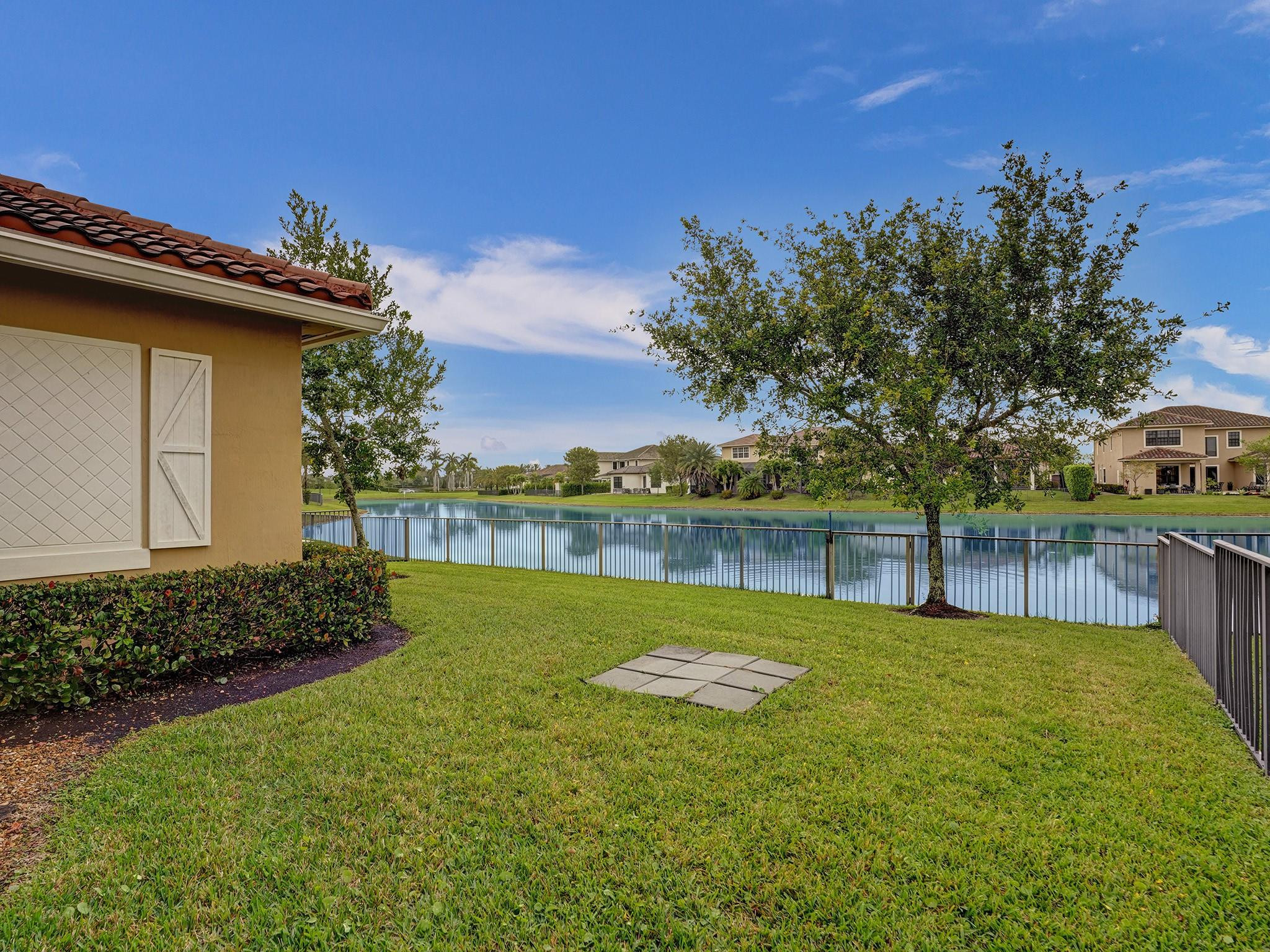 Lakeside backyard with a broad lawn, metal railing, and neighboring homes across the water.