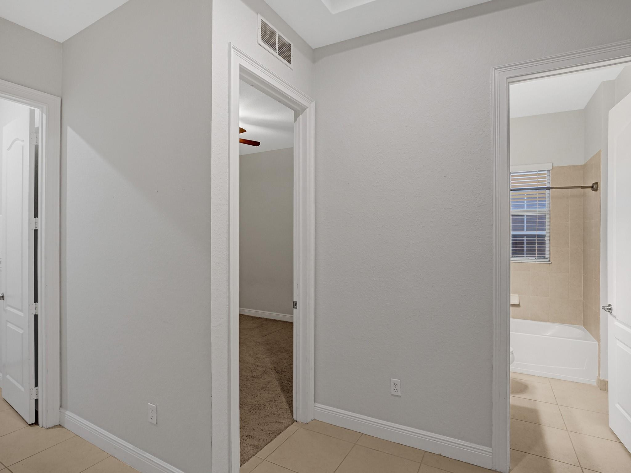 Tiled hallway with open doorways to a bathtub bathroom and carpeted room.