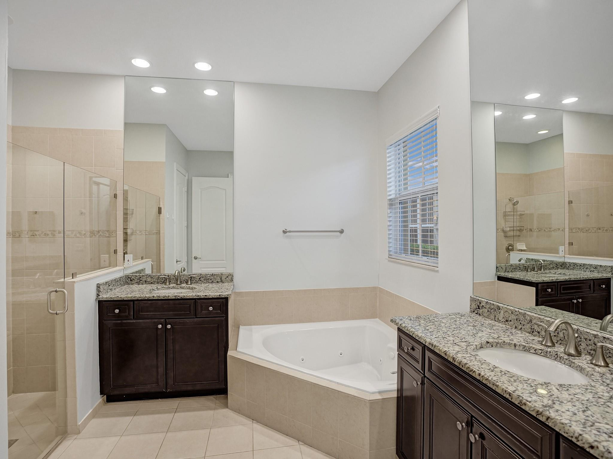 Bathroom with a corner jetted tub, glass shower, and two granite-topped vanities.