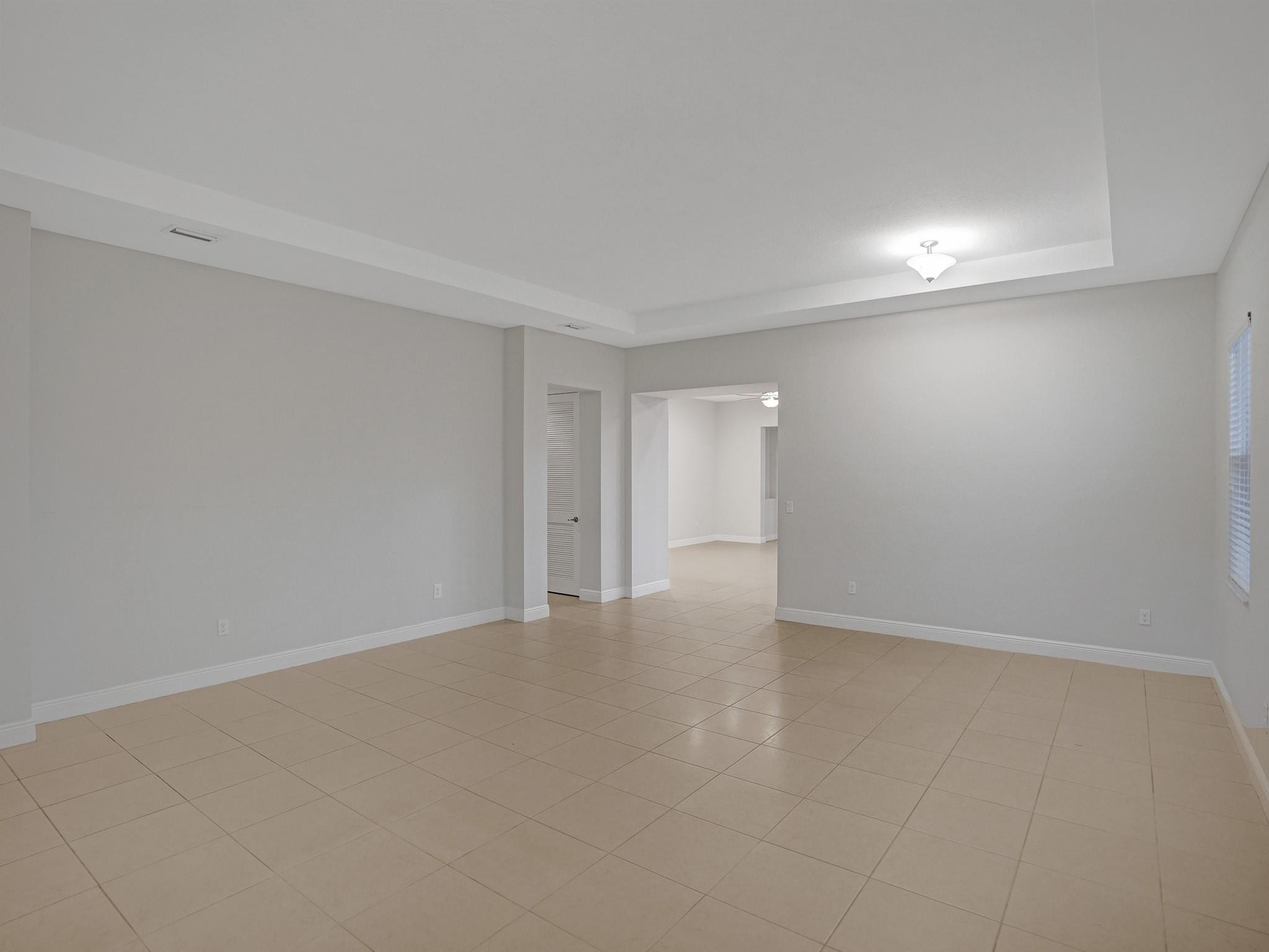 Empty living area with beige tile floors, a tray ceiling, and an opening to an adjoining room.