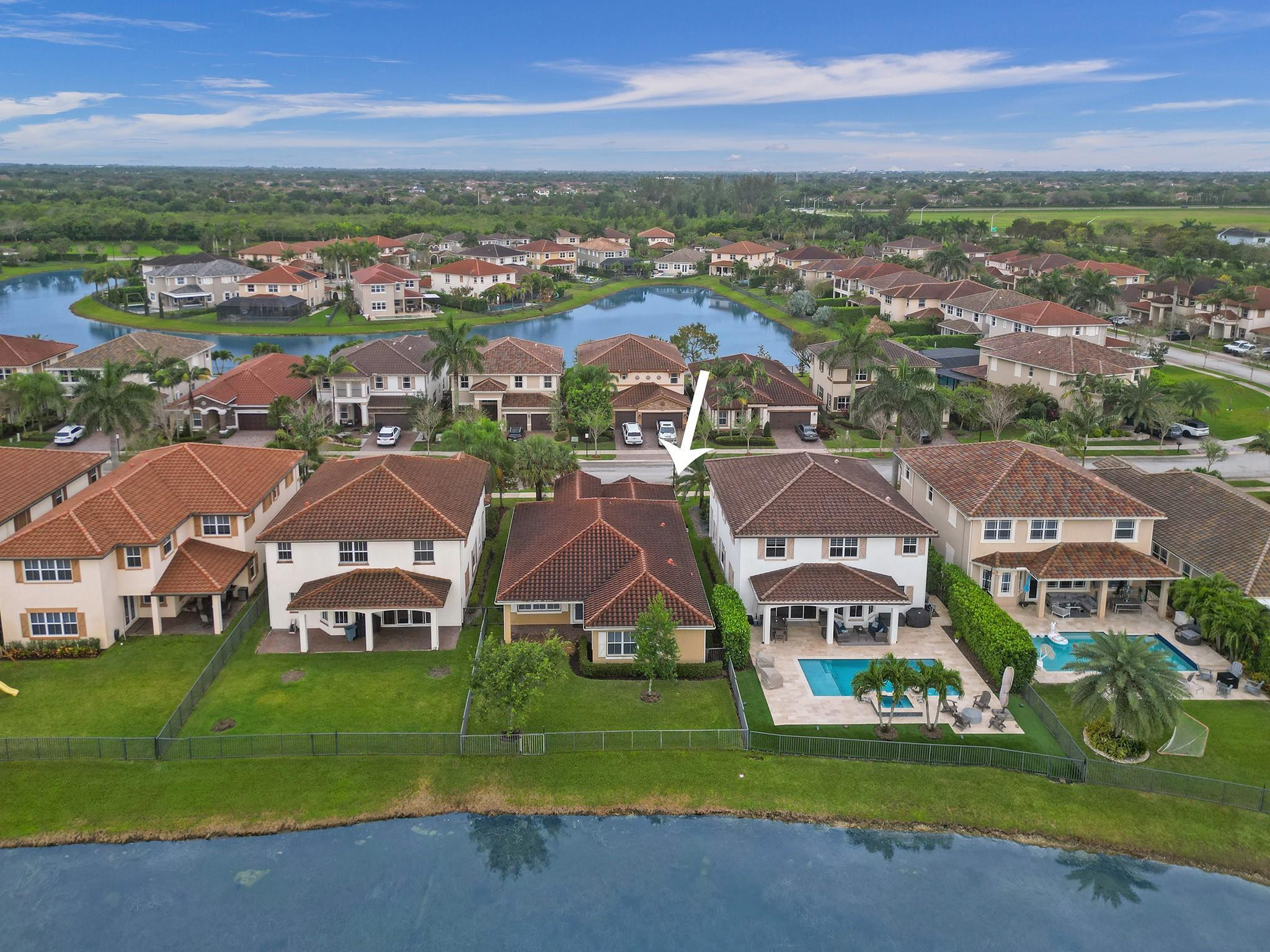 Aerial view of an arrow-marked home beside a lake, surrounded by tiled-roof houses.