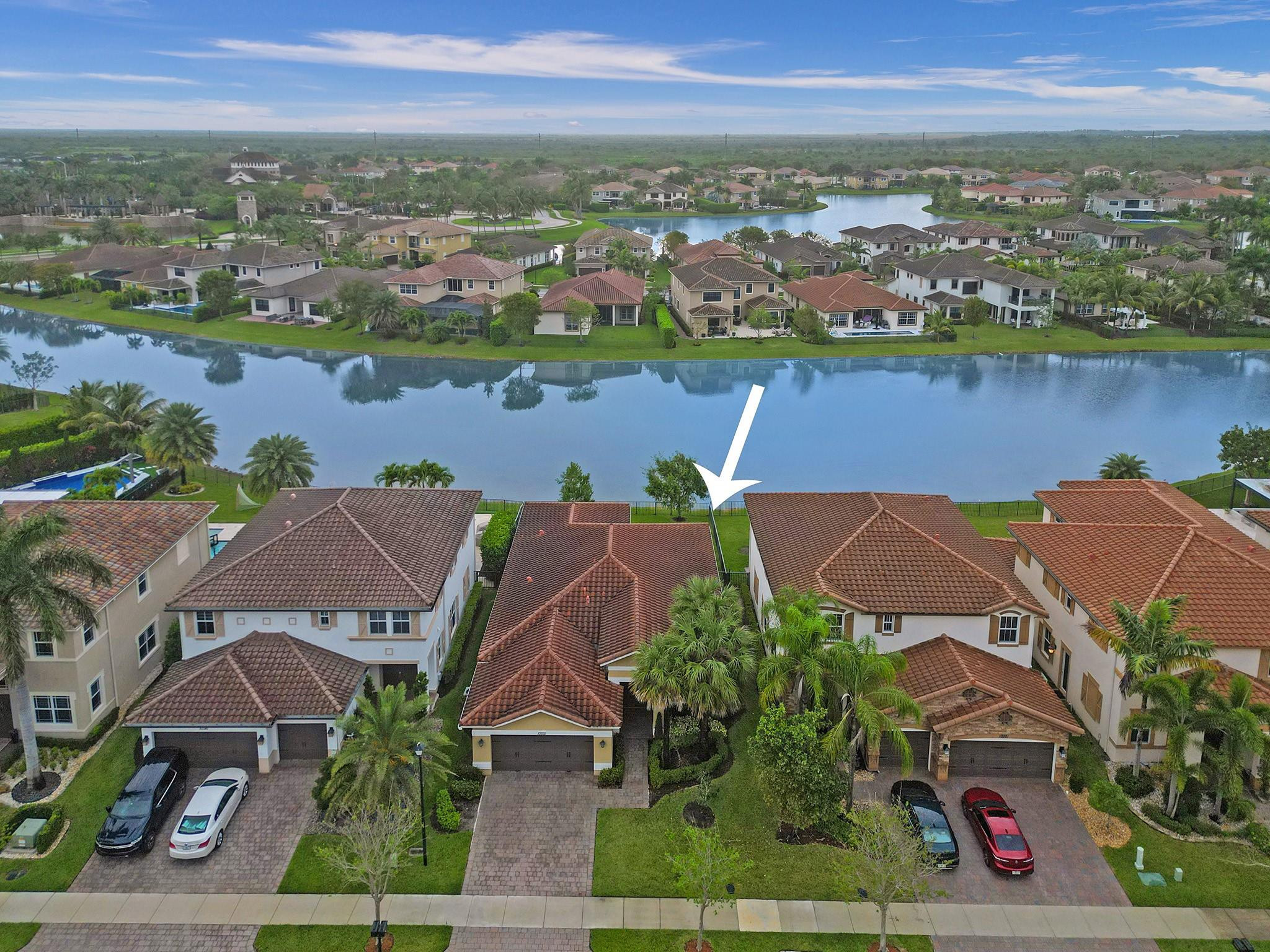 Aerial view of the indicated tile-roofed home beside a lake in a palm-lined neighborhood.