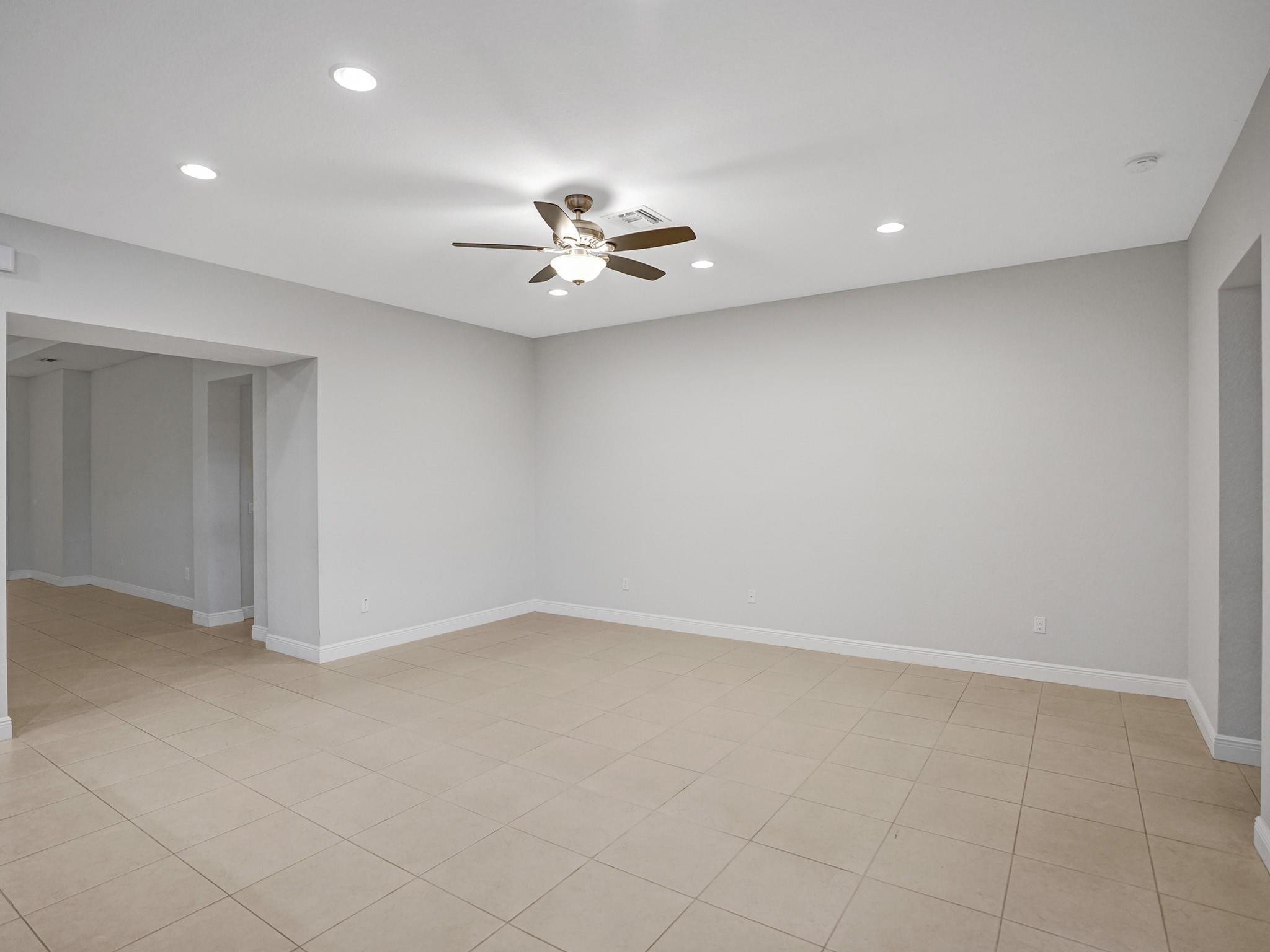 Empty tiled room with gray walls, recessed lights, and a ceiling fan.