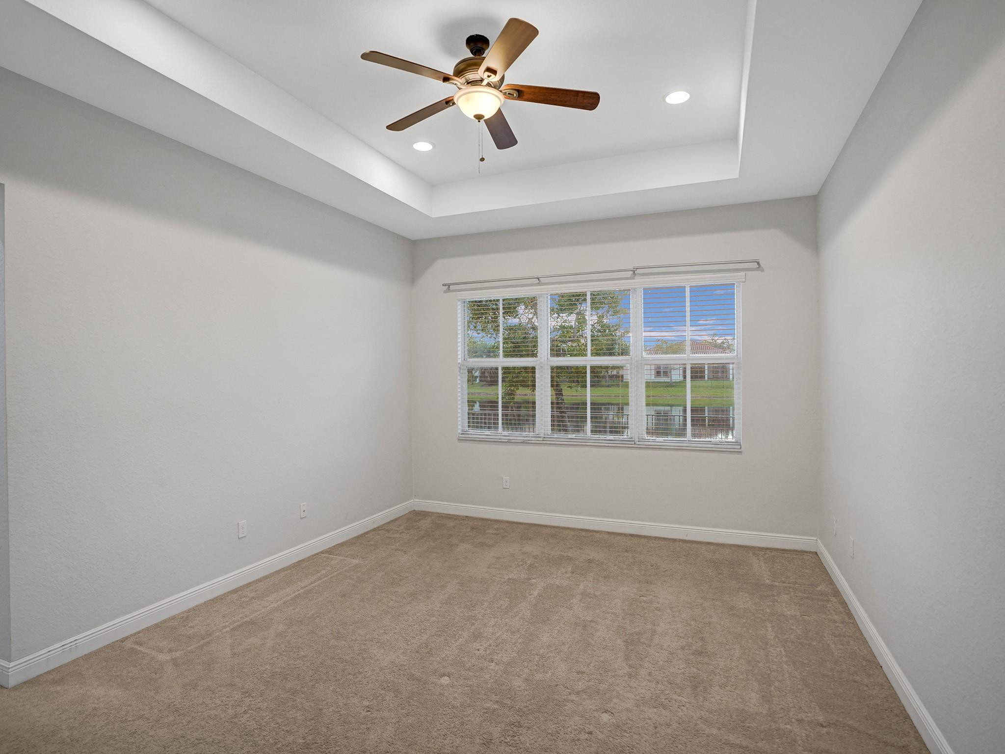 Empty bedroom with beige carpet, a large window, and a wood-blade ceiling fan.