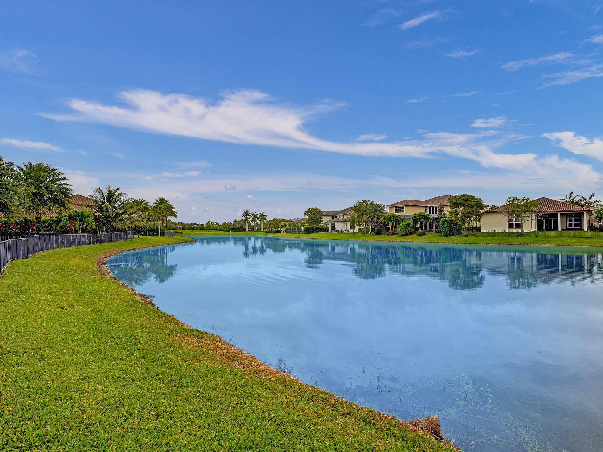 Neighborhood lake bordered by lawns and palm trees, with homes reflected across the water.