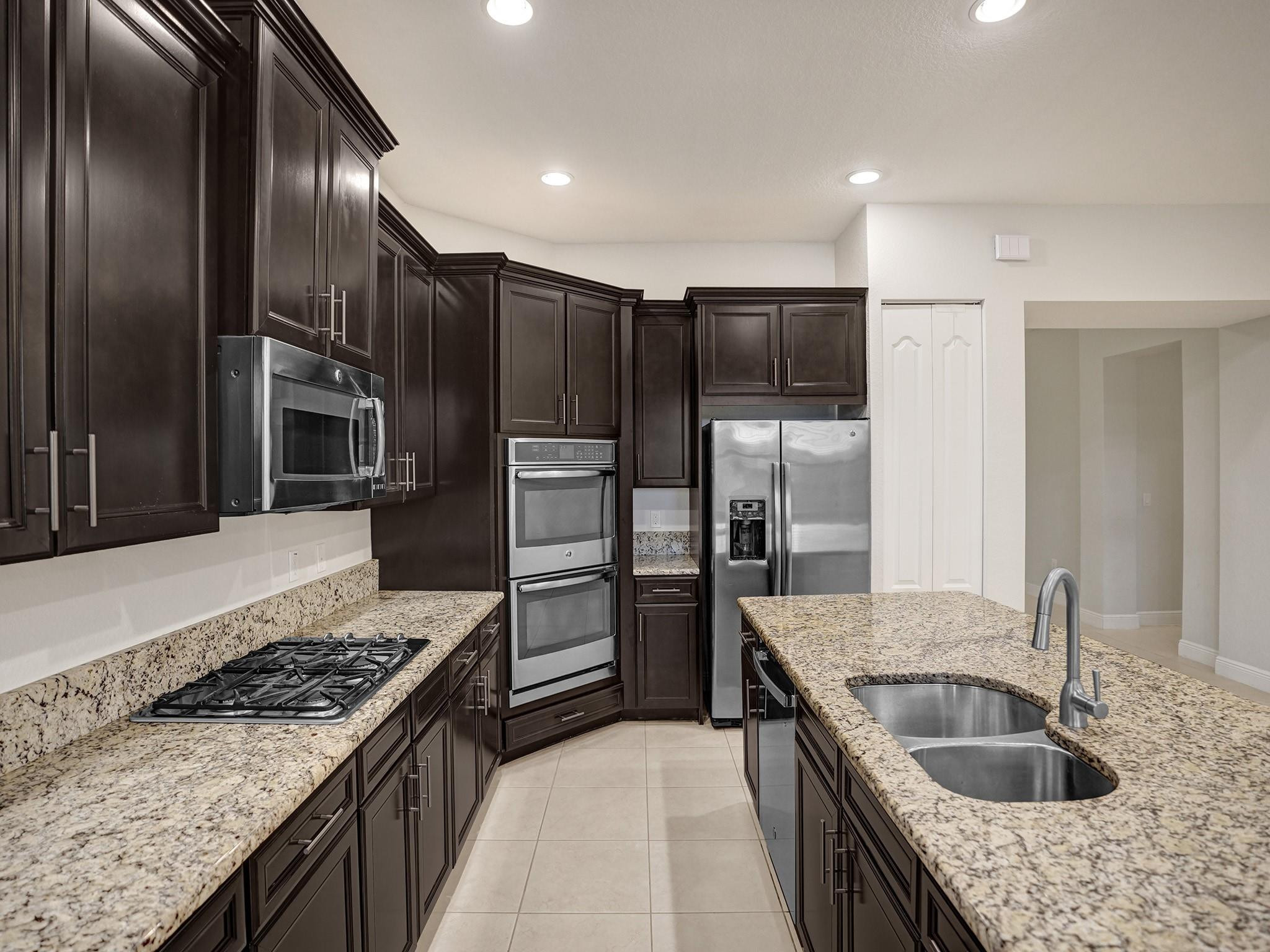 Kitchen with dark wood cabinets, granite counters, stainless appliances, and a large island sink.