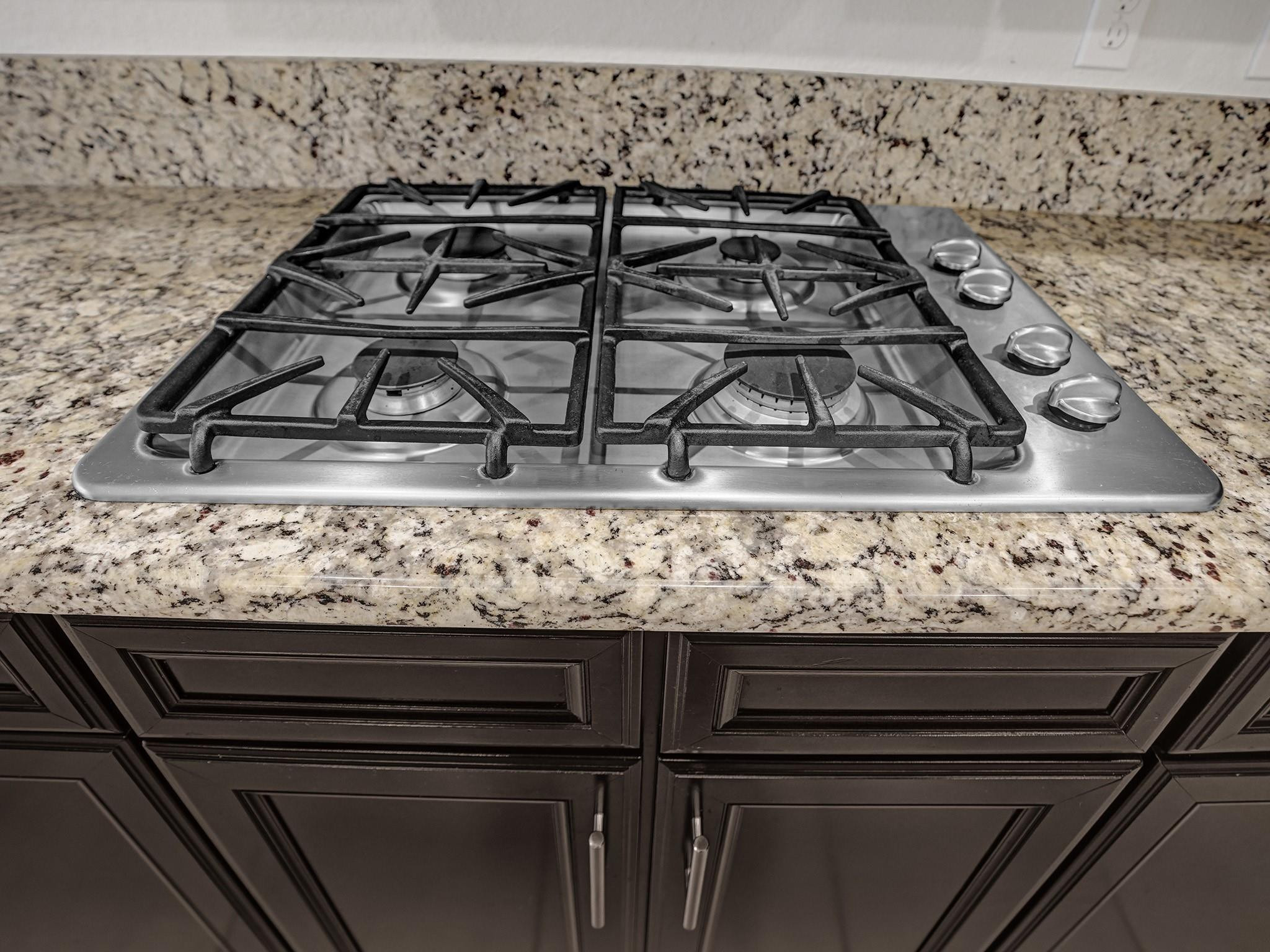 Four-burner gas cooktop set into speckled granite counters above dark kitchen cabinets.