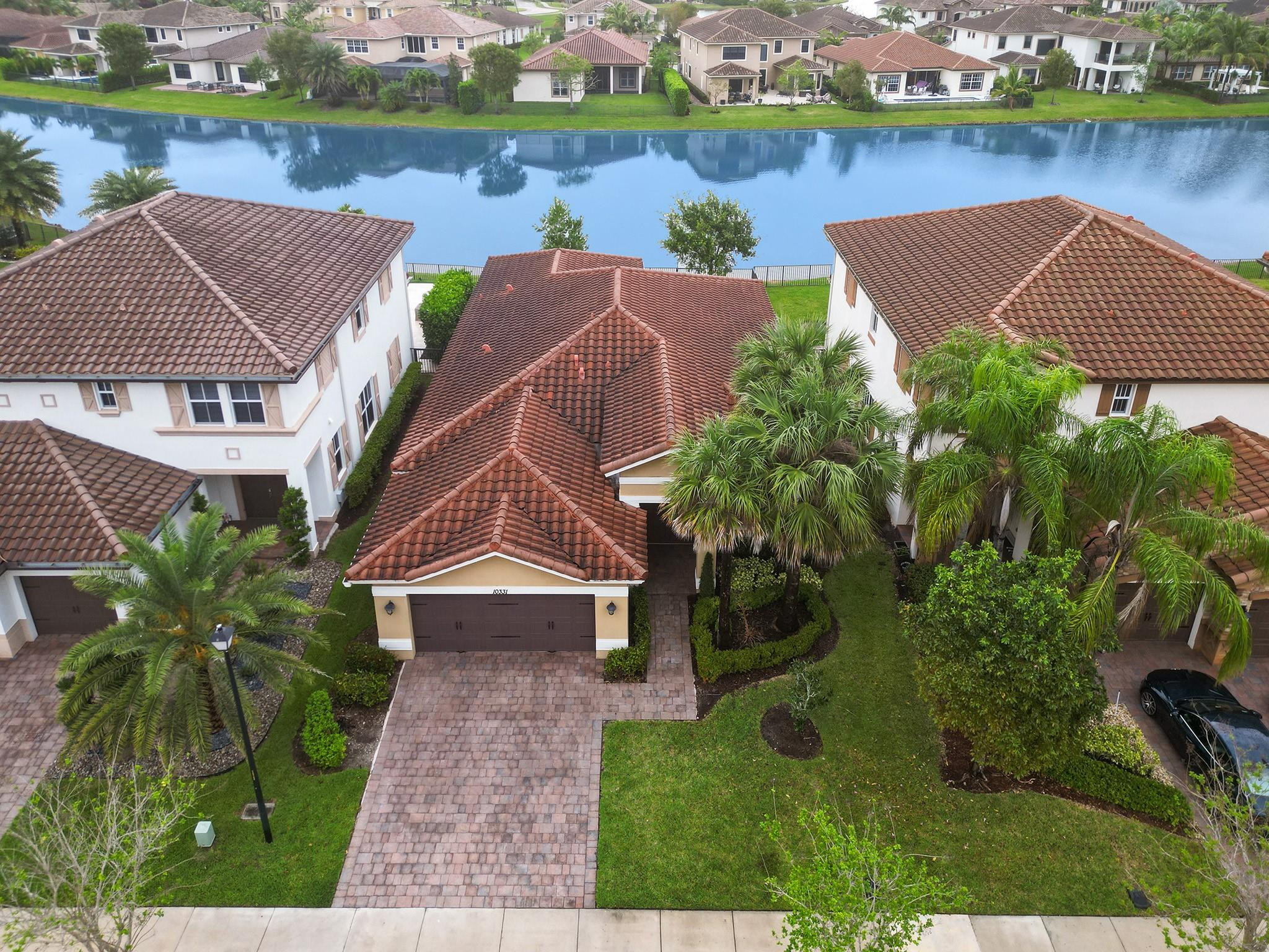 Aerial view of a tiled-roof home, landscaped driveway, palm trees, and lakefront neighborhood.
