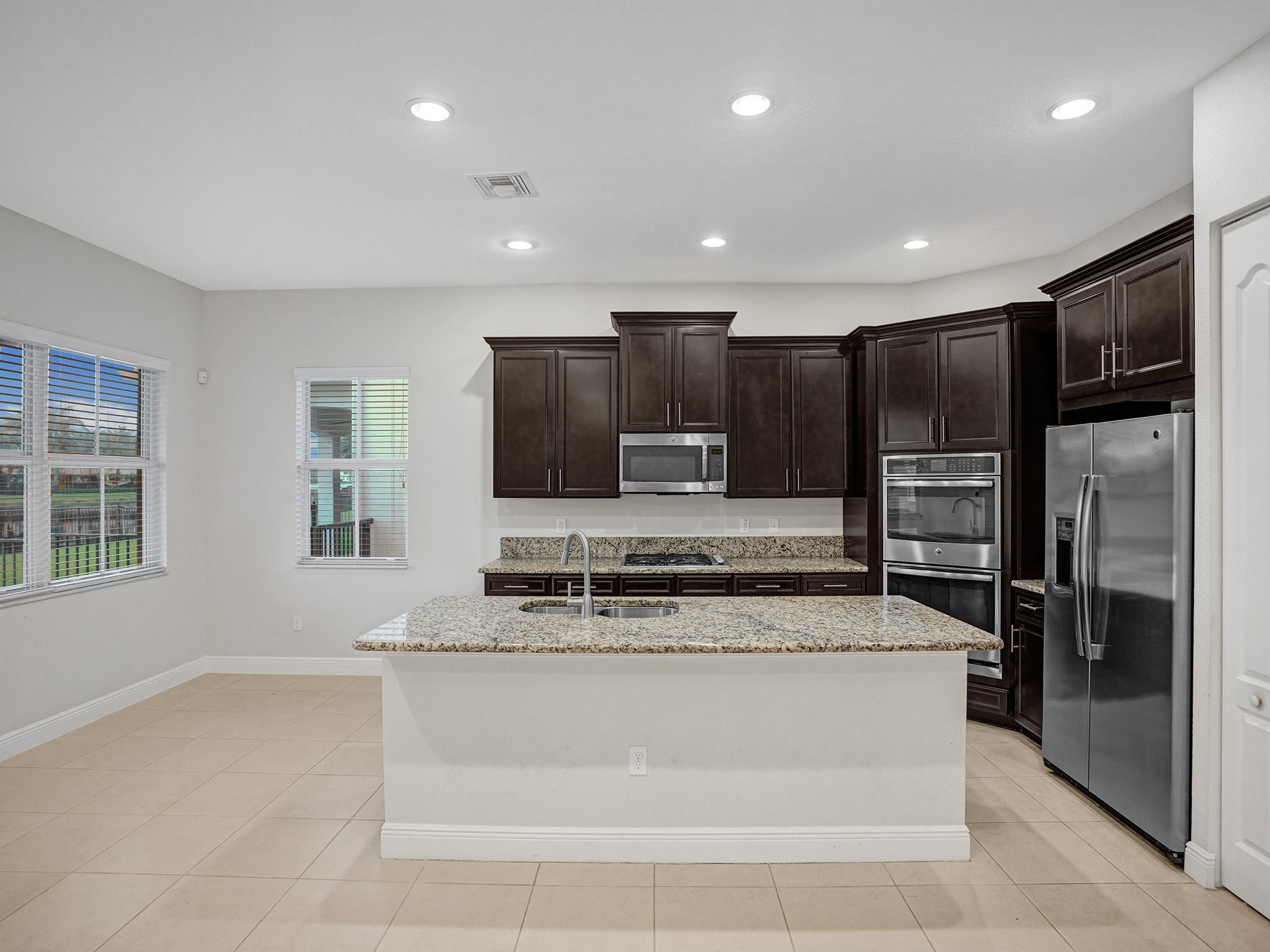 Kitchen with dark cabinets, granite island and countertops, and stainless steel appliances.