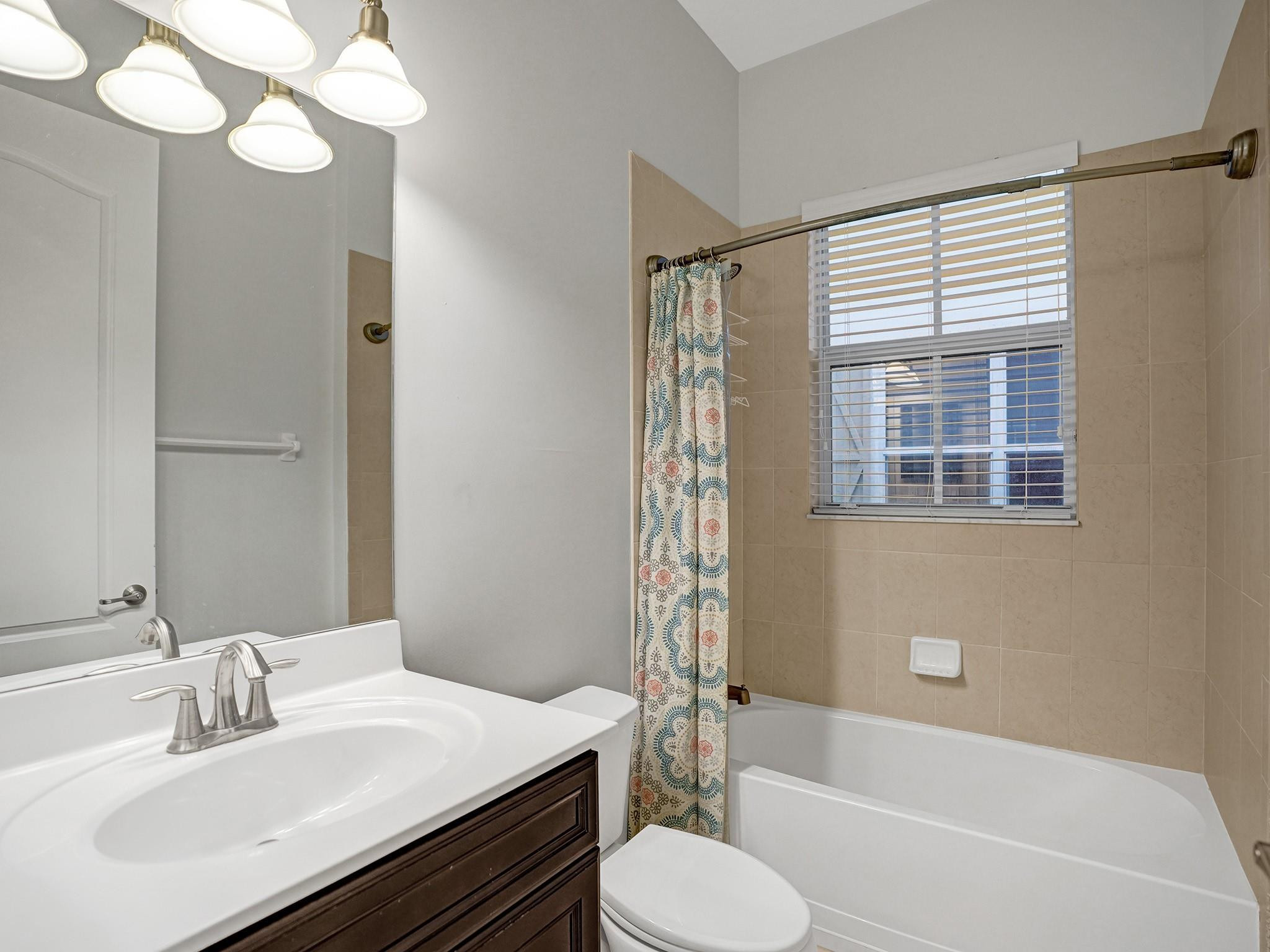 Bathroom with a white tub, patterned shower curtain, and sink with dark wood vanity.