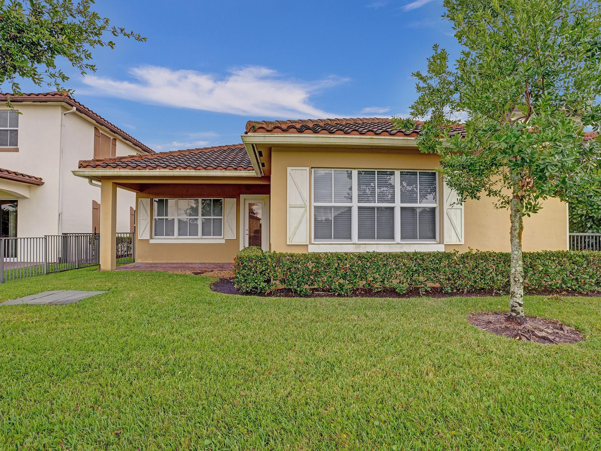 Tan home with a terracotta tile roof, covered entry, white shutters, and broad front lawn.