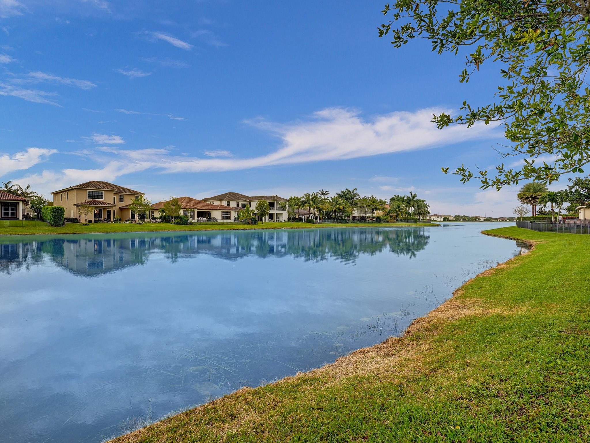 Waterfront homes reflected in a calm lake beside a grassy shoreline.