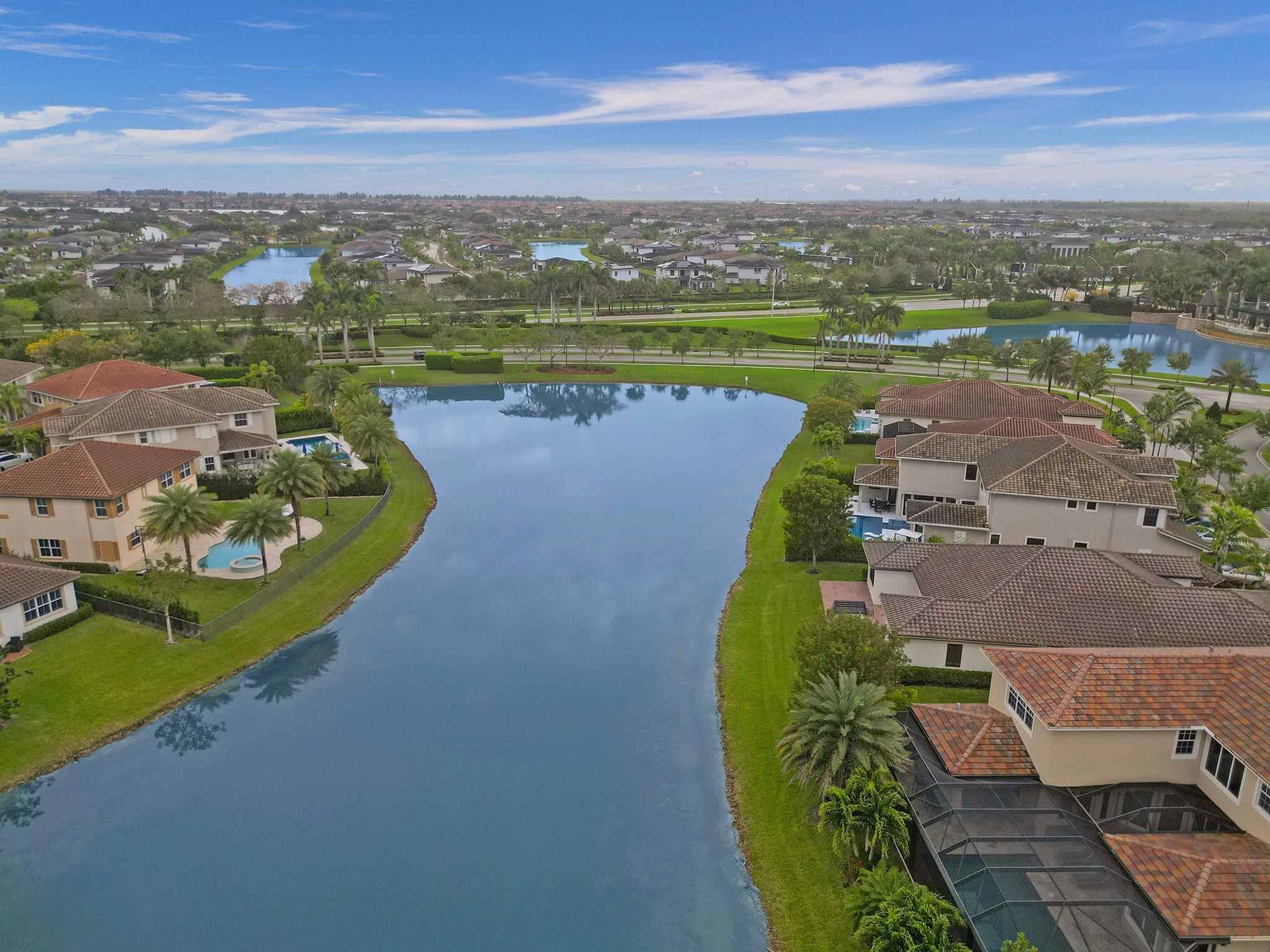 Aerial neighborhood view of a broad lake bordered by homes, palms, and green lawns.