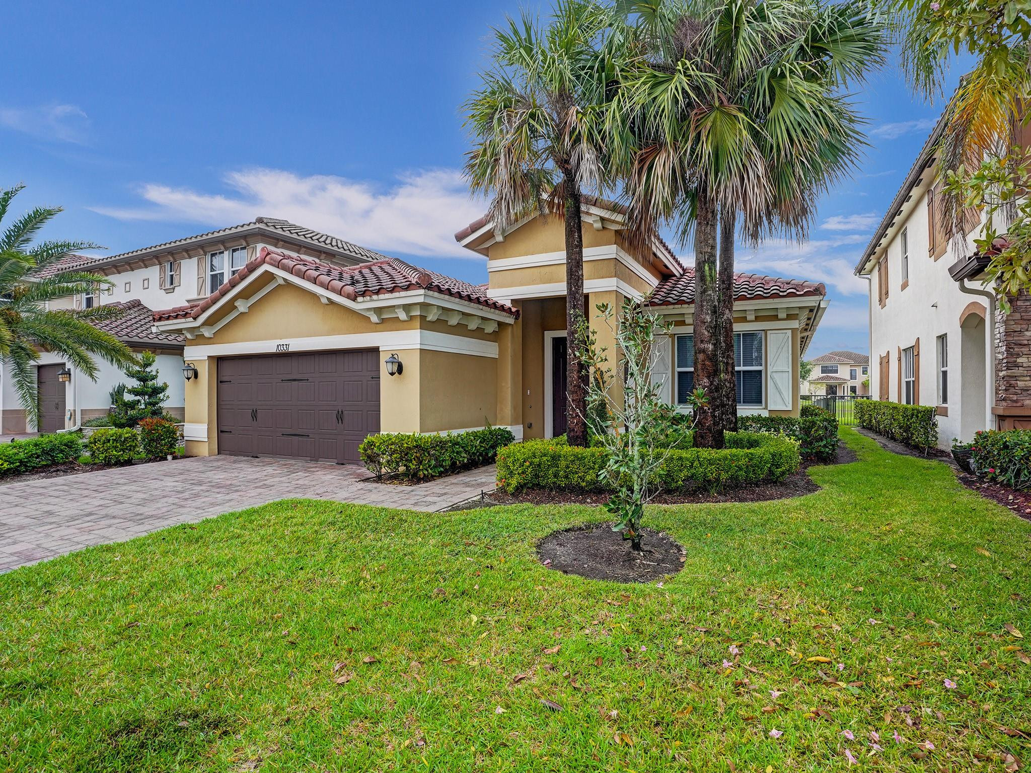 Tan stucco home with a red tile roof, double garage, and palm trees in front.