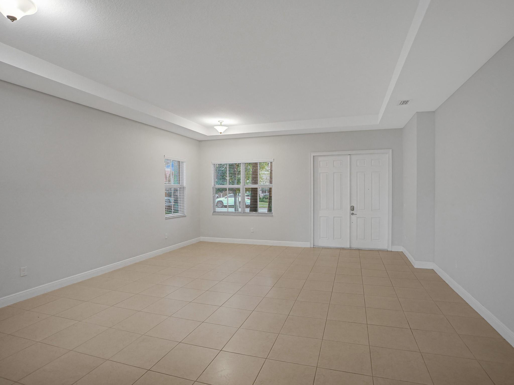 Empty tiled room with a tray ceiling, two windows, and double doors.