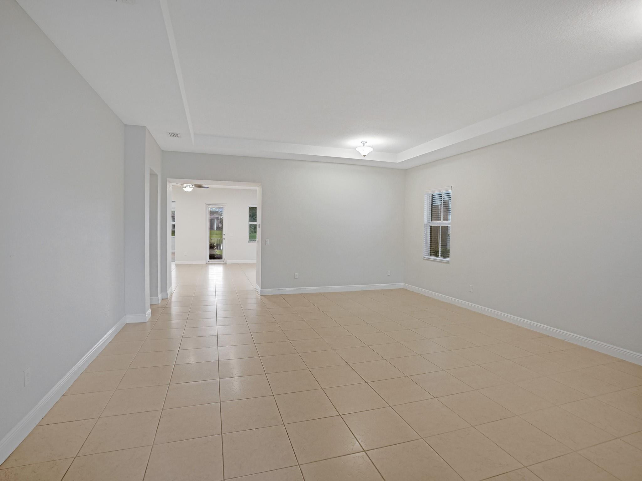 Vacant living room with beige tile floors, a tray ceiling, and an opening to an adjoining room.