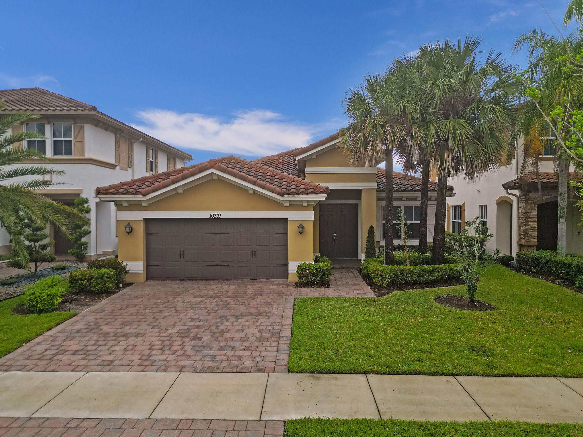 Two-story home with terracotta tile roofs, a two-car garage, paver driveway, and palm-lined front yard.