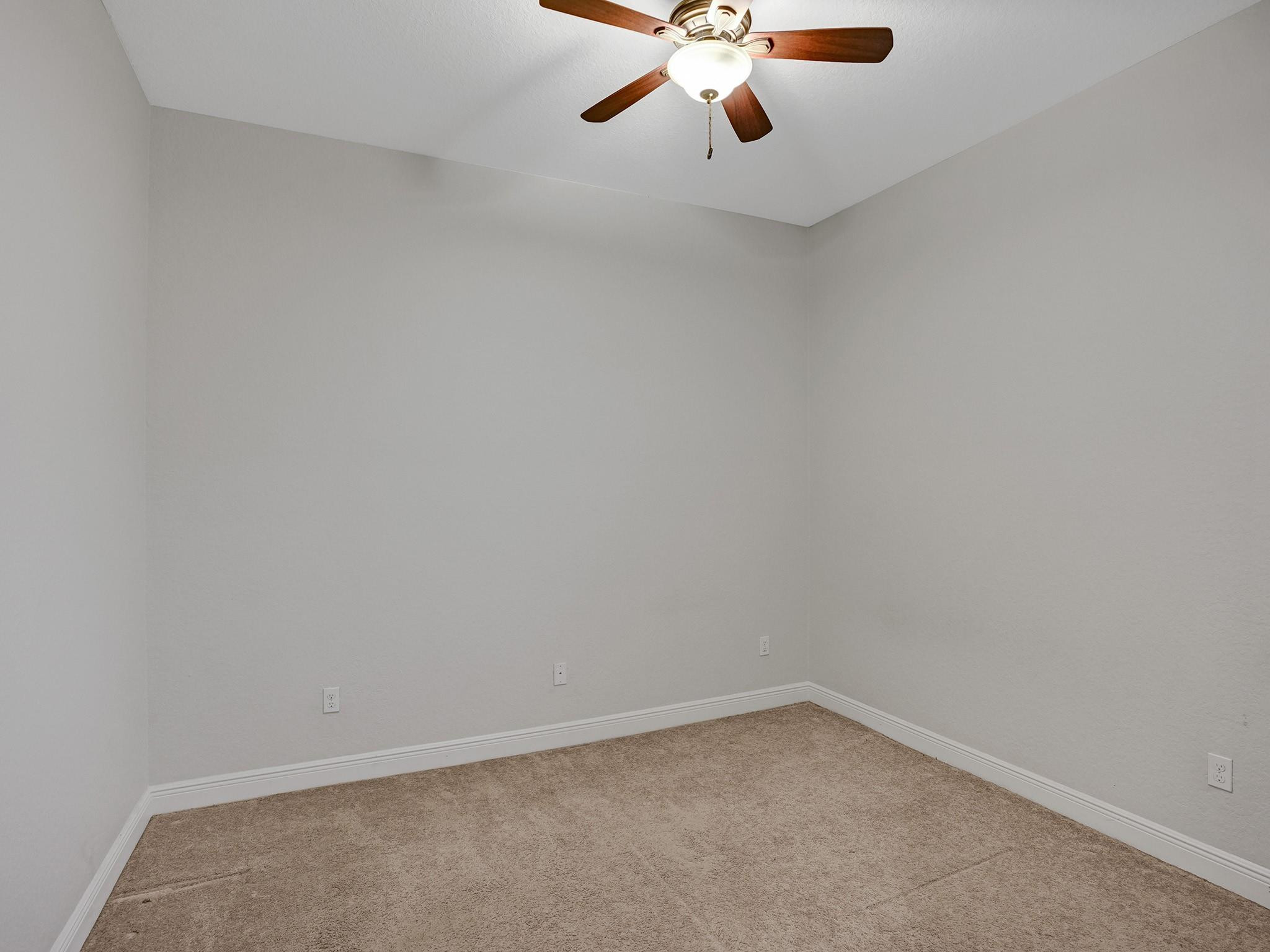 Vacant carpeted room with gray walls and a ceiling fan with light.