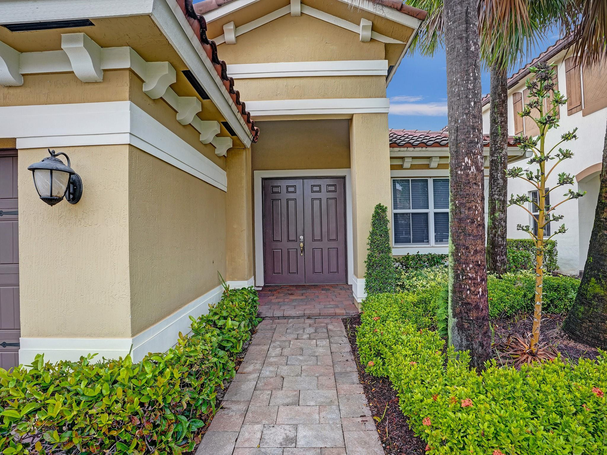 Home entrance with dark double doors, a covered porch, and a brick-paver path through landscaped shrubs.