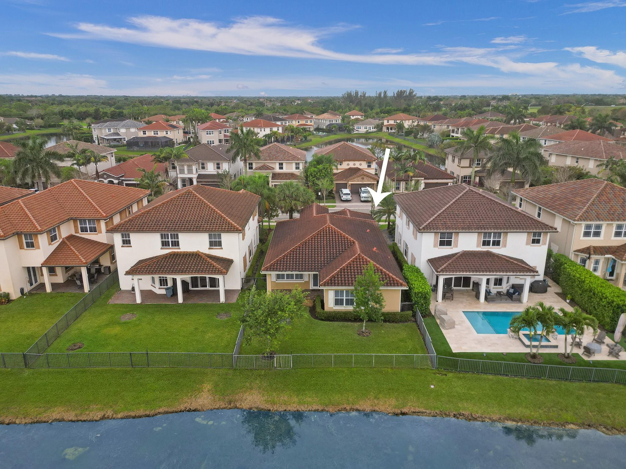Aerial view of the tile-roofed house marked by an arrow, beside a pond in a suburban neighborhood.