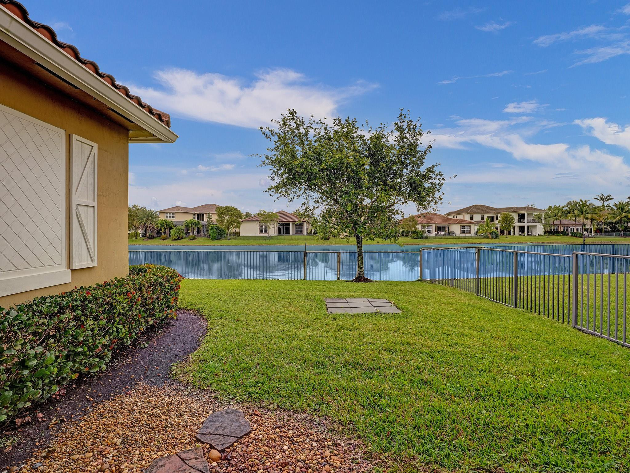 Lakeside backyard with a fenced lawn, mature tree, and neighboring homes across the water.