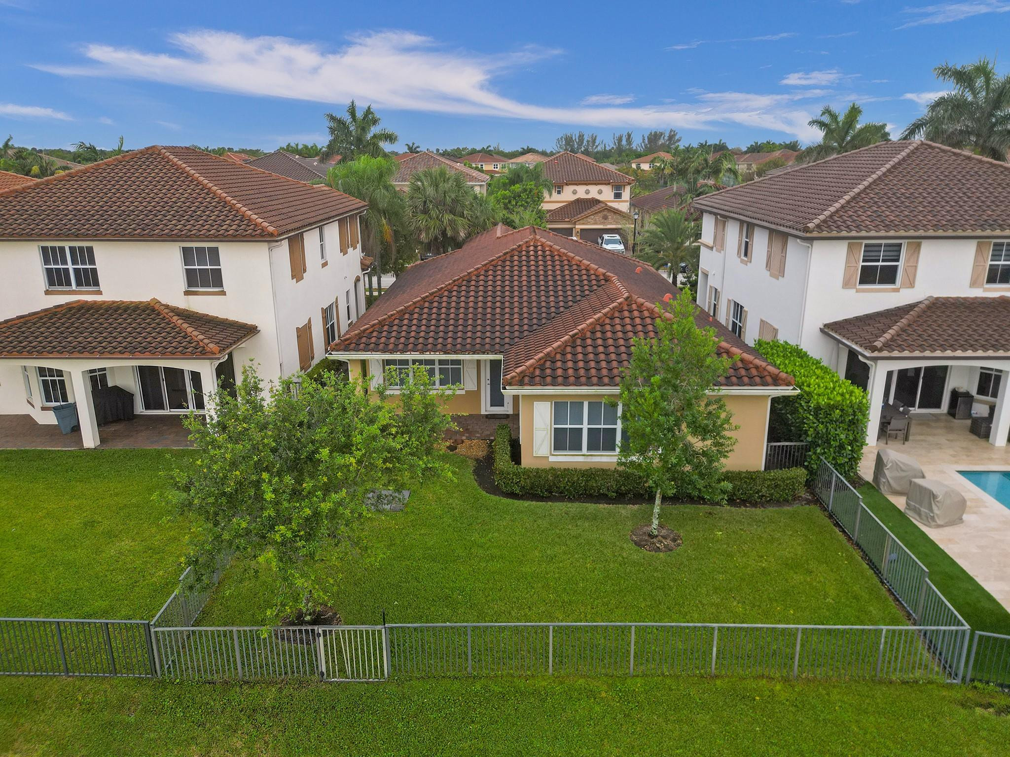 Aerial view of the home's terracotta-tile rear roof, fenced lawn, and landscaped yard beside a pool.