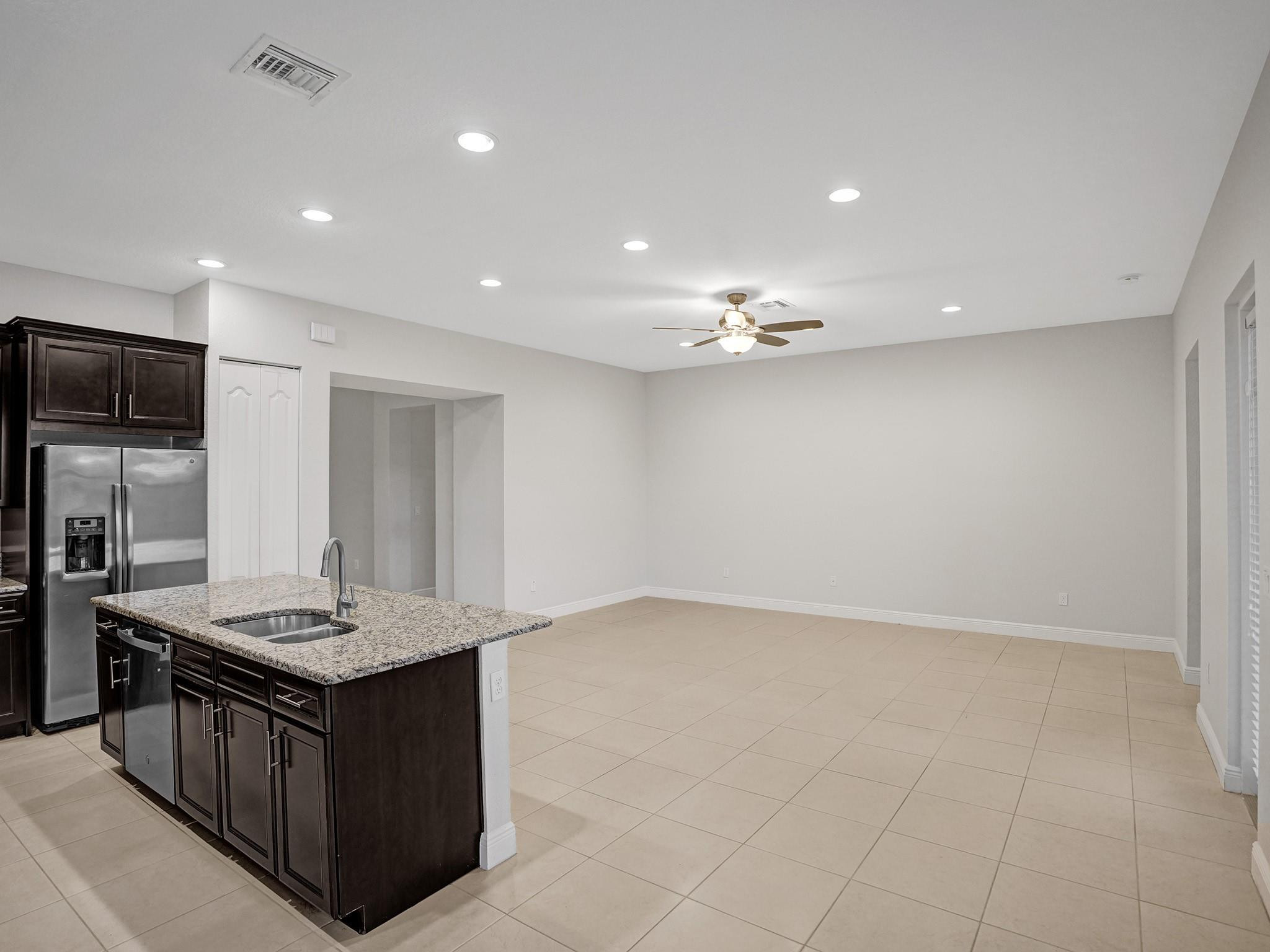 Kitchen and open living area with dark cabinets, granite island, stainless appliances, and light tile flooring.