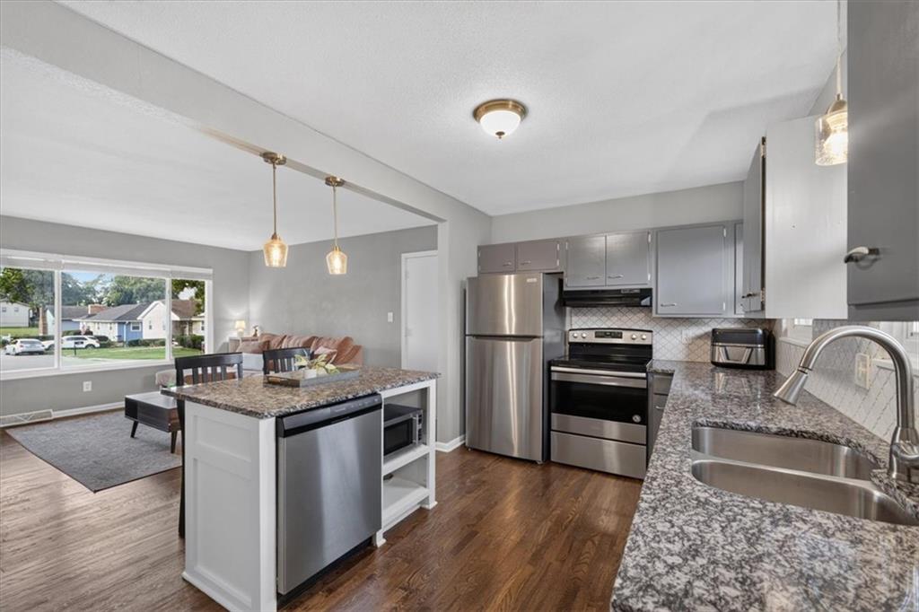 Open-plan kitchen with stainless steel appliances, granite counters, and a white island beside the living area.