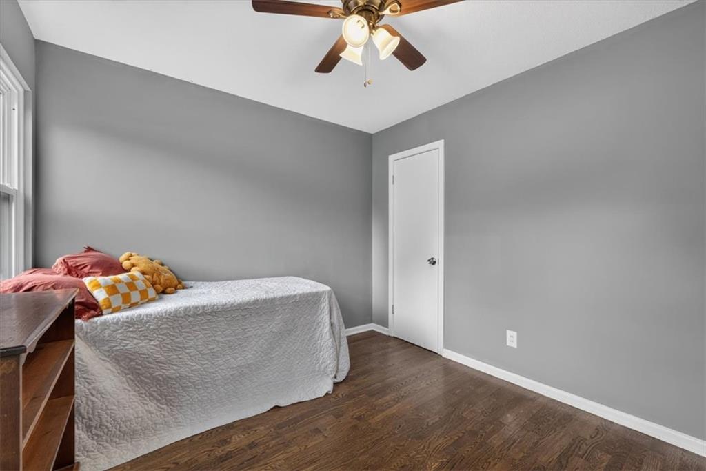 Bedroom with gray walls, dark wood floors, and a bed beneath a ceiling fan.