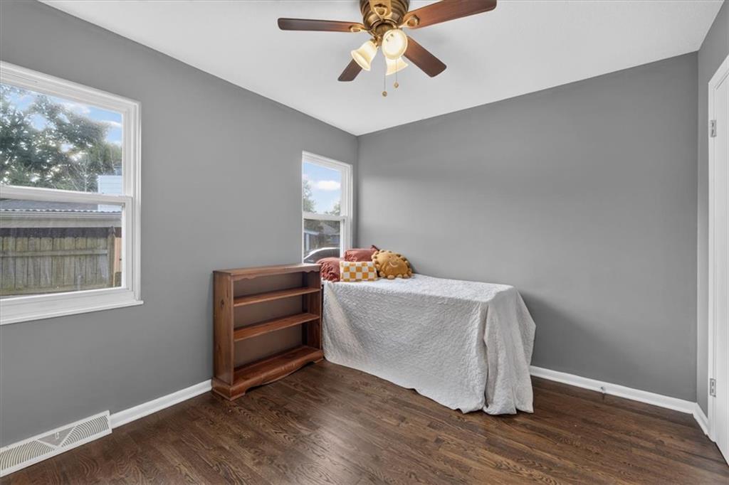 Bedroom with gray walls, dark wood floors, two windows, and a single bed beside a wooden bookshelf.