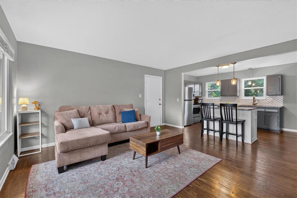 Open-plan living room and kitchen with a pink sectional, patterned rug, and island seating.
