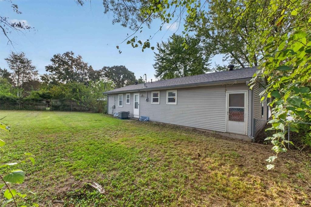 Rear of a single-story gray-sided house beside a broad grassy backyard and fence.