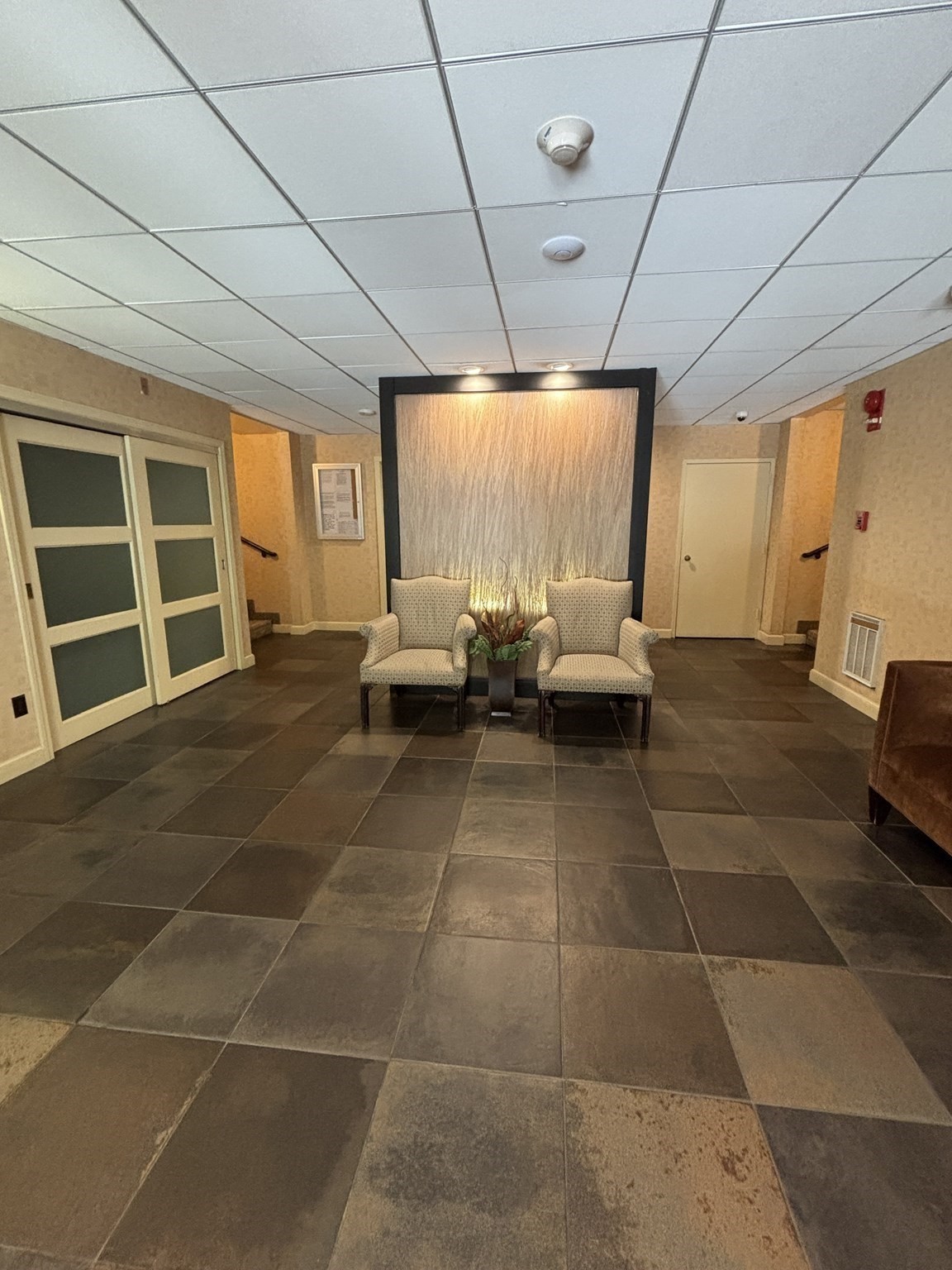Building lobby with two chairs, a planter, and a lit wood accent wall.