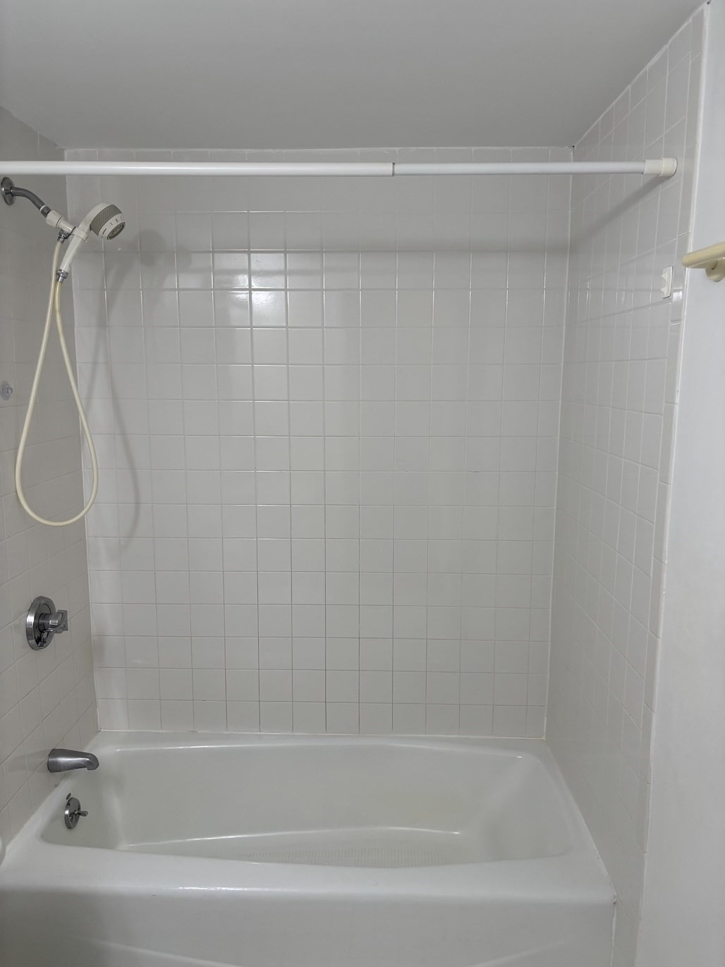 White bathtub and tiled shower with a handheld showerhead and curtain rod.