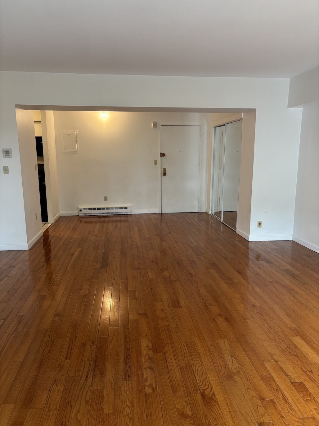 Unfurnished living room with polished hardwood floors and mirrored closet doors.