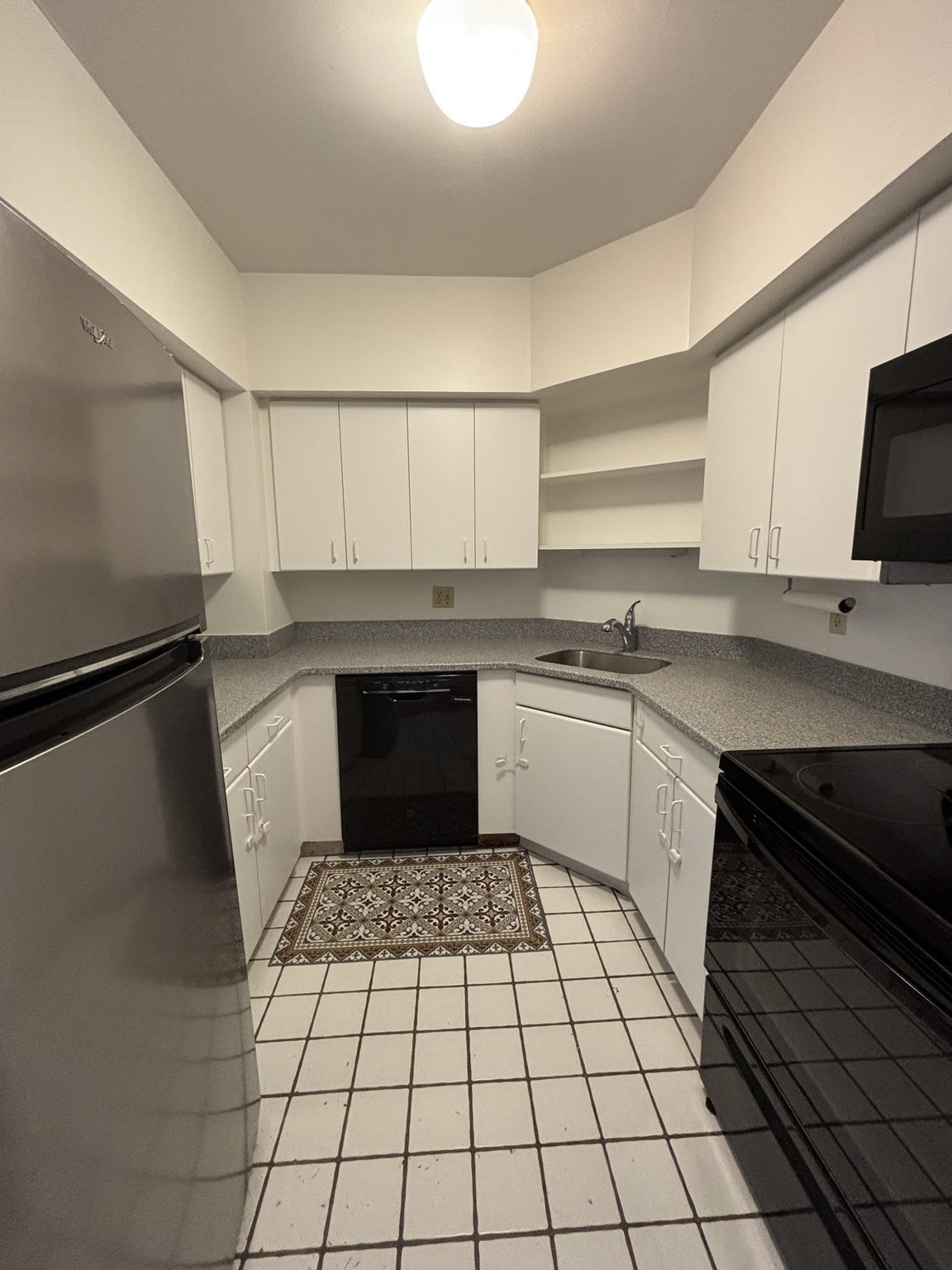Compact U-shaped kitchen with white cabinets, gray countertops, and a patterned floor mat.