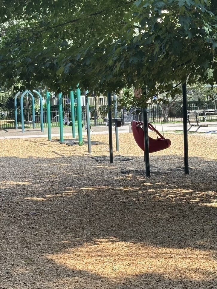 Playground with turquoise swings and a red bucket swing under leafy trees.