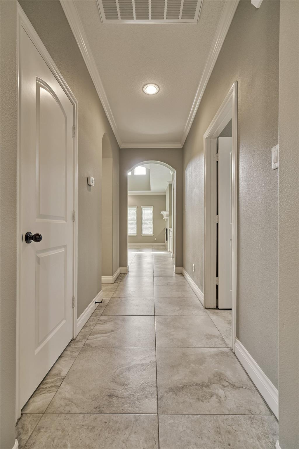 Empty hallway with large stone-look tile floors and an arched opening to a bright room.