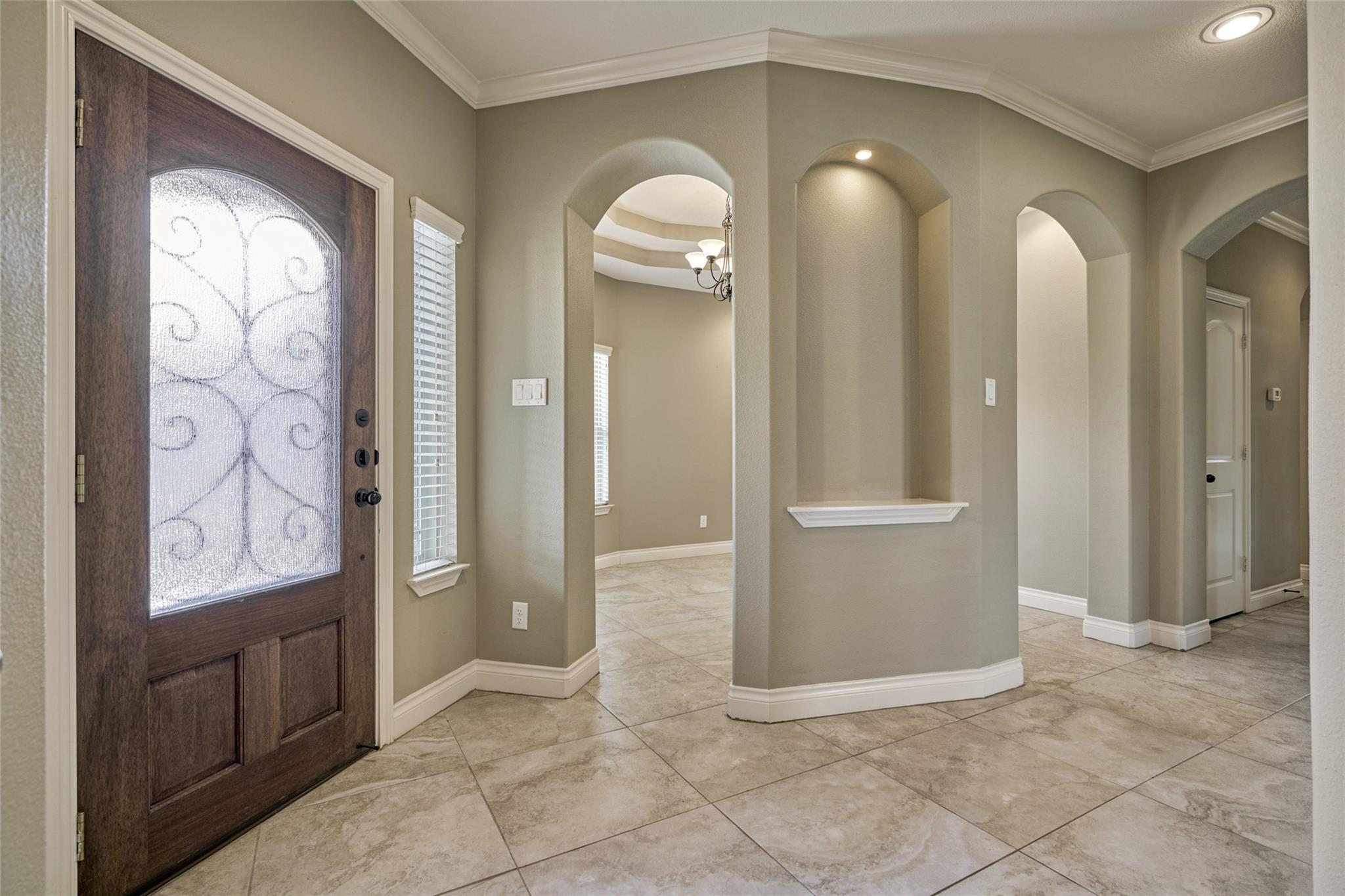 Foyer with a frosted-glass wood entry door, tiled floor, and multiple arched openings.