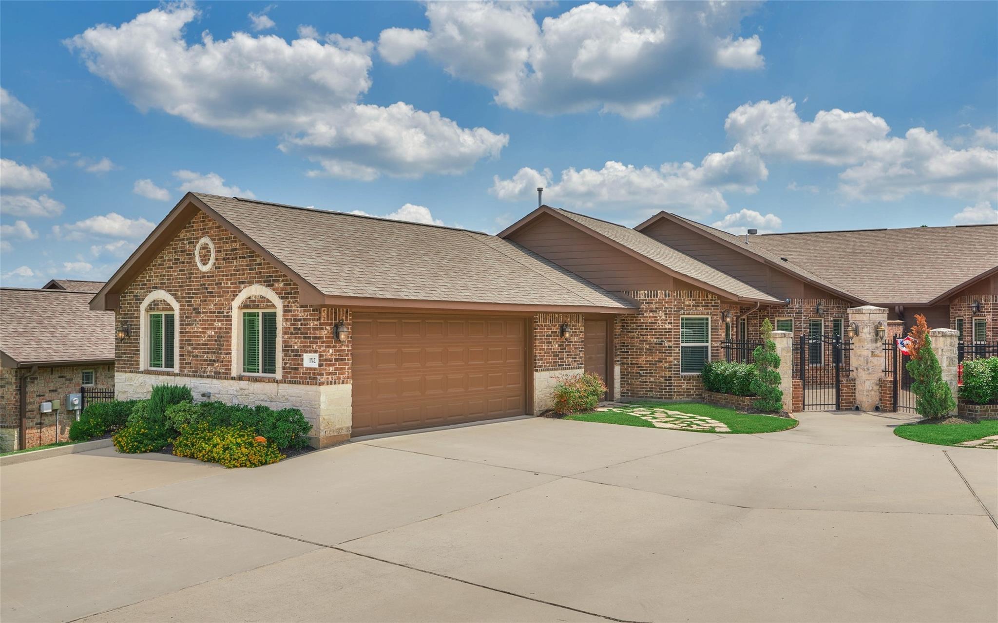 Brick home with an attached garage, arched windows, landscaped shrubs, and a gated entry.