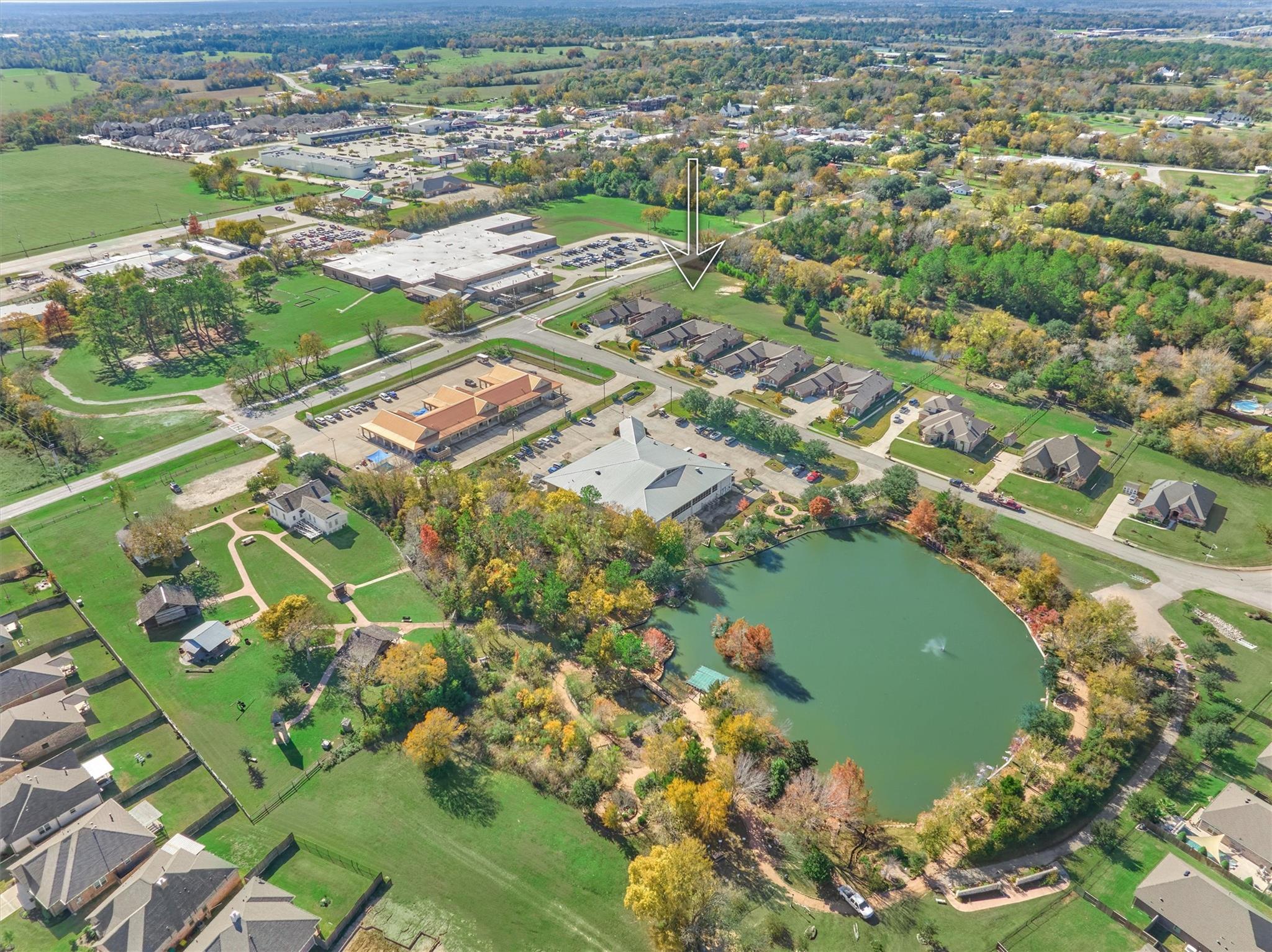 Aerial view of the arrow-marked house beside a wooded pond and neighborhood homes.