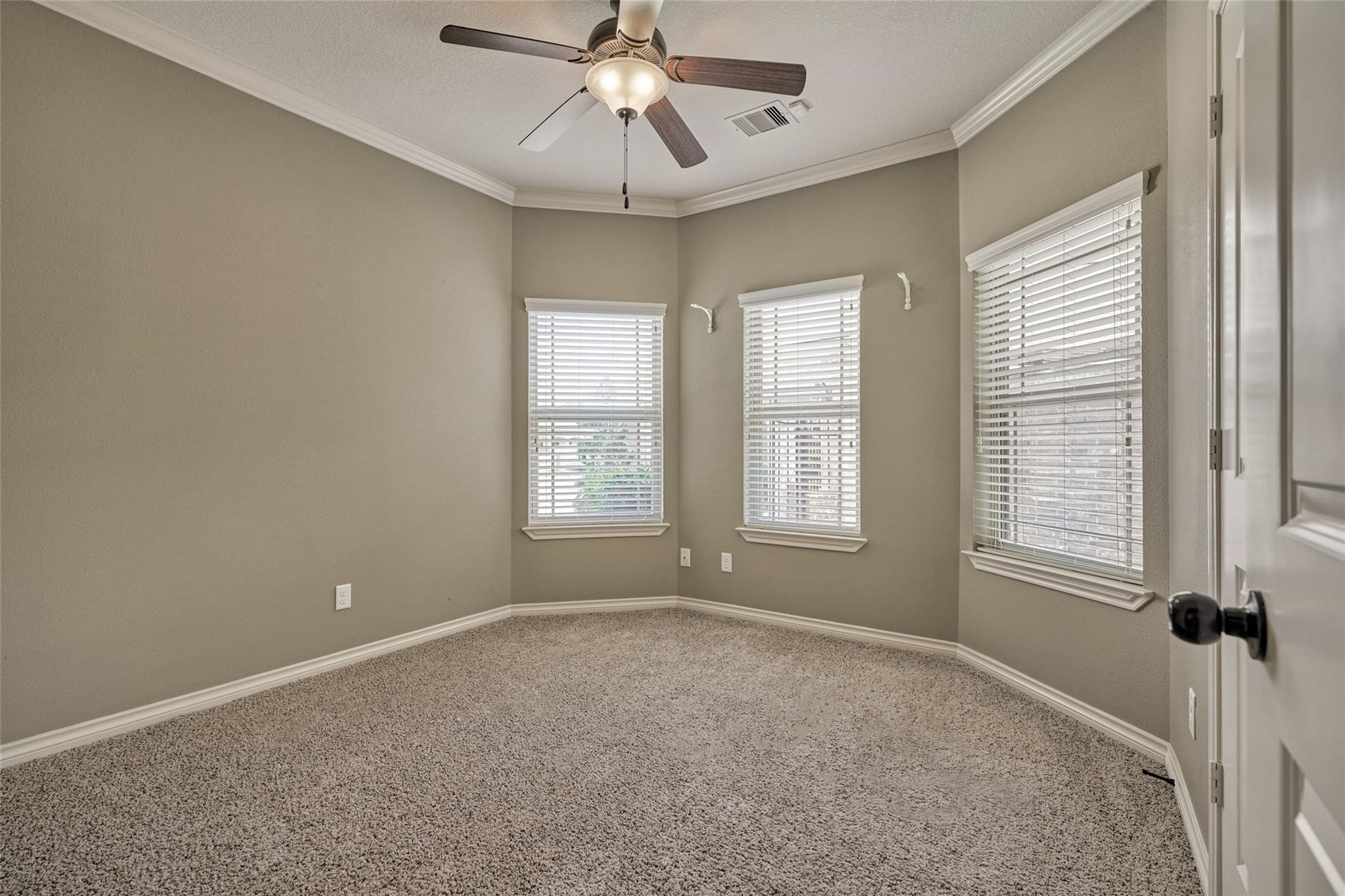 Empty carpeted room with three windows, white blinds, and a ceiling fan.