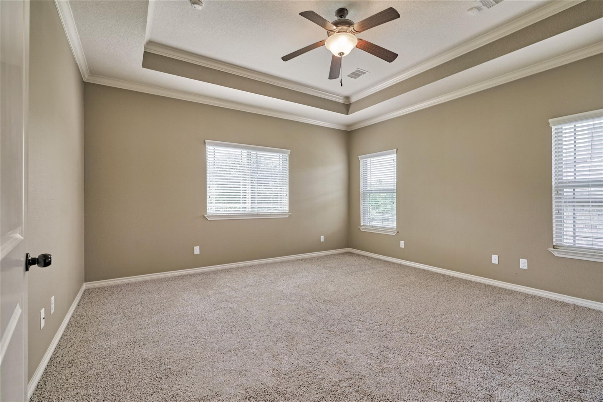 Empty carpeted bedroom with three windows, white blinds, and a lit ceiling fan.