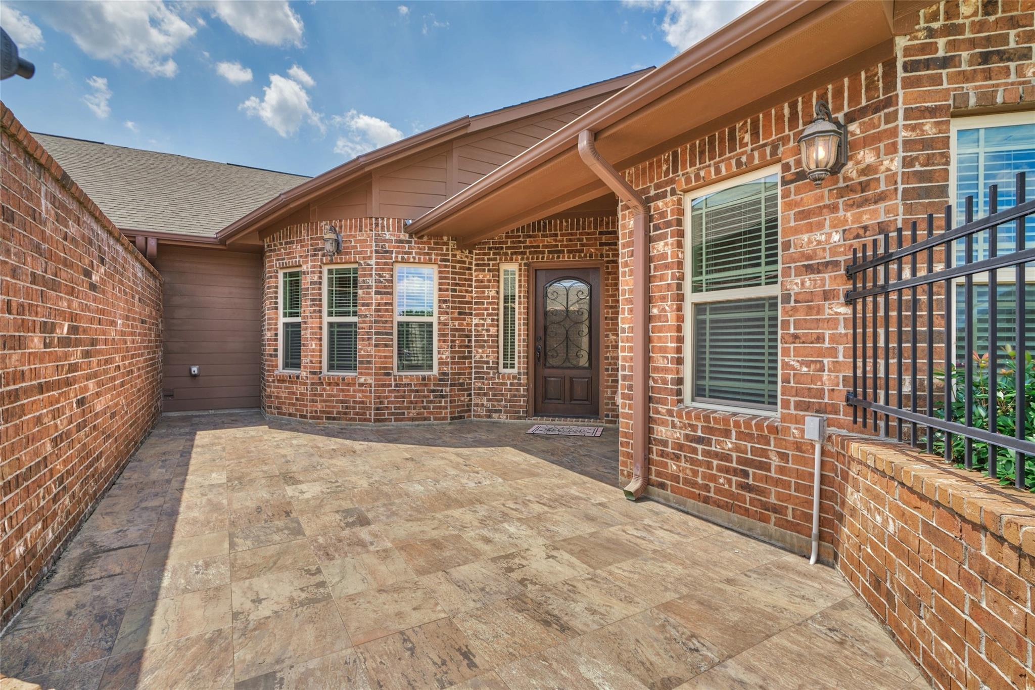 Brick home’s covered front entry and broad tiled courtyard with a decorative dark door.