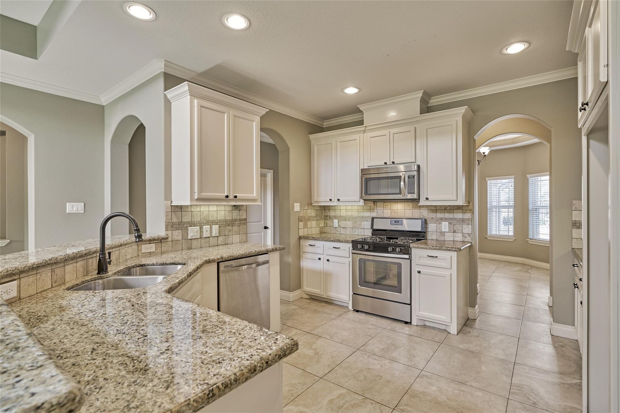Kitchen with white cabinets, granite counters, stainless steel appliances, and an arched doorway to an adjoining room.