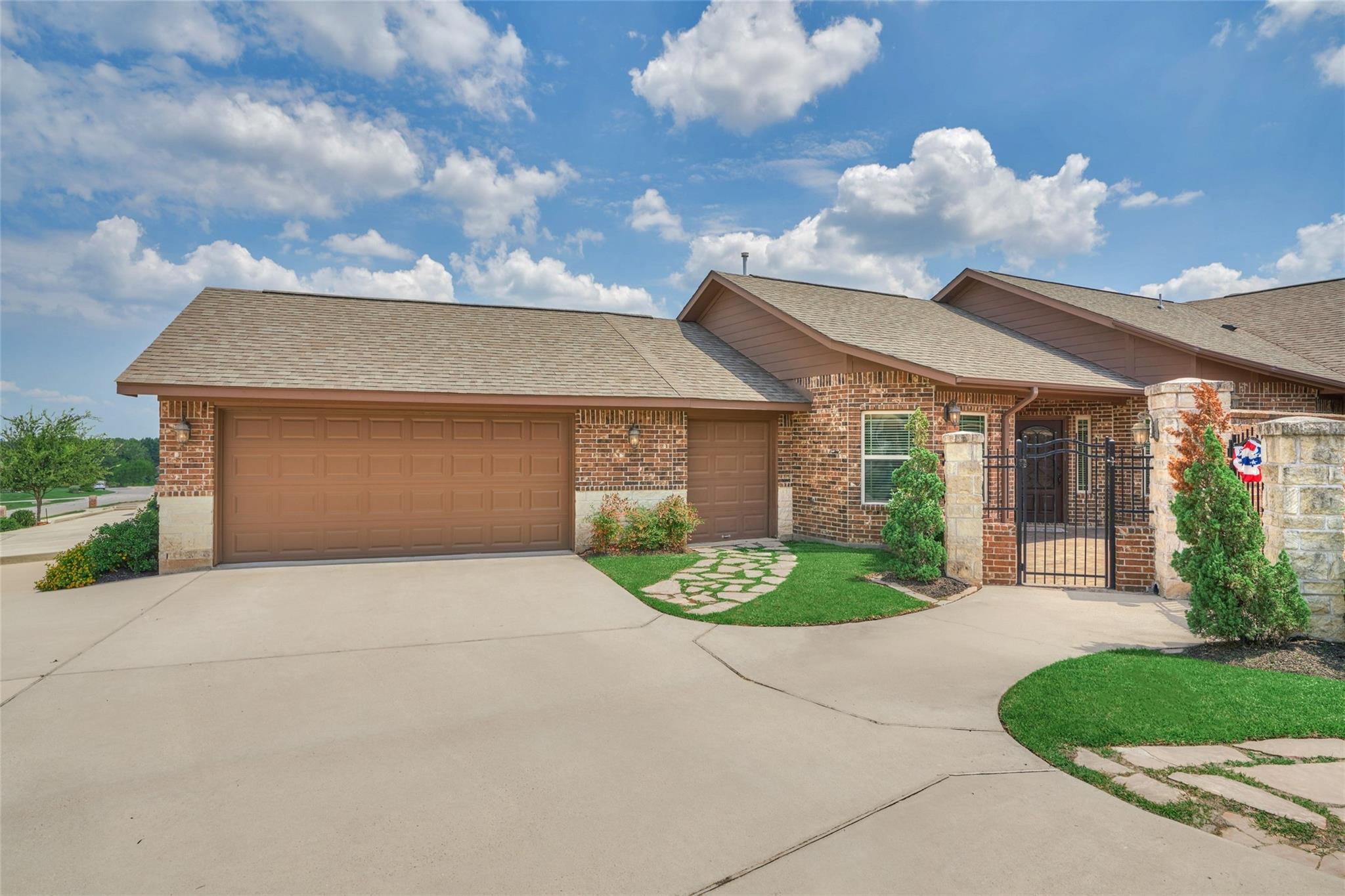 Brick home with two garage doors, a wide driveway, stone entry columns, and a gated front entrance.