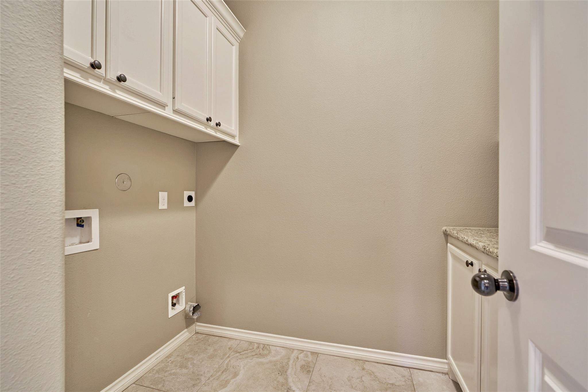 Empty laundry room with white cabinets, granite counter, and washer hookups.