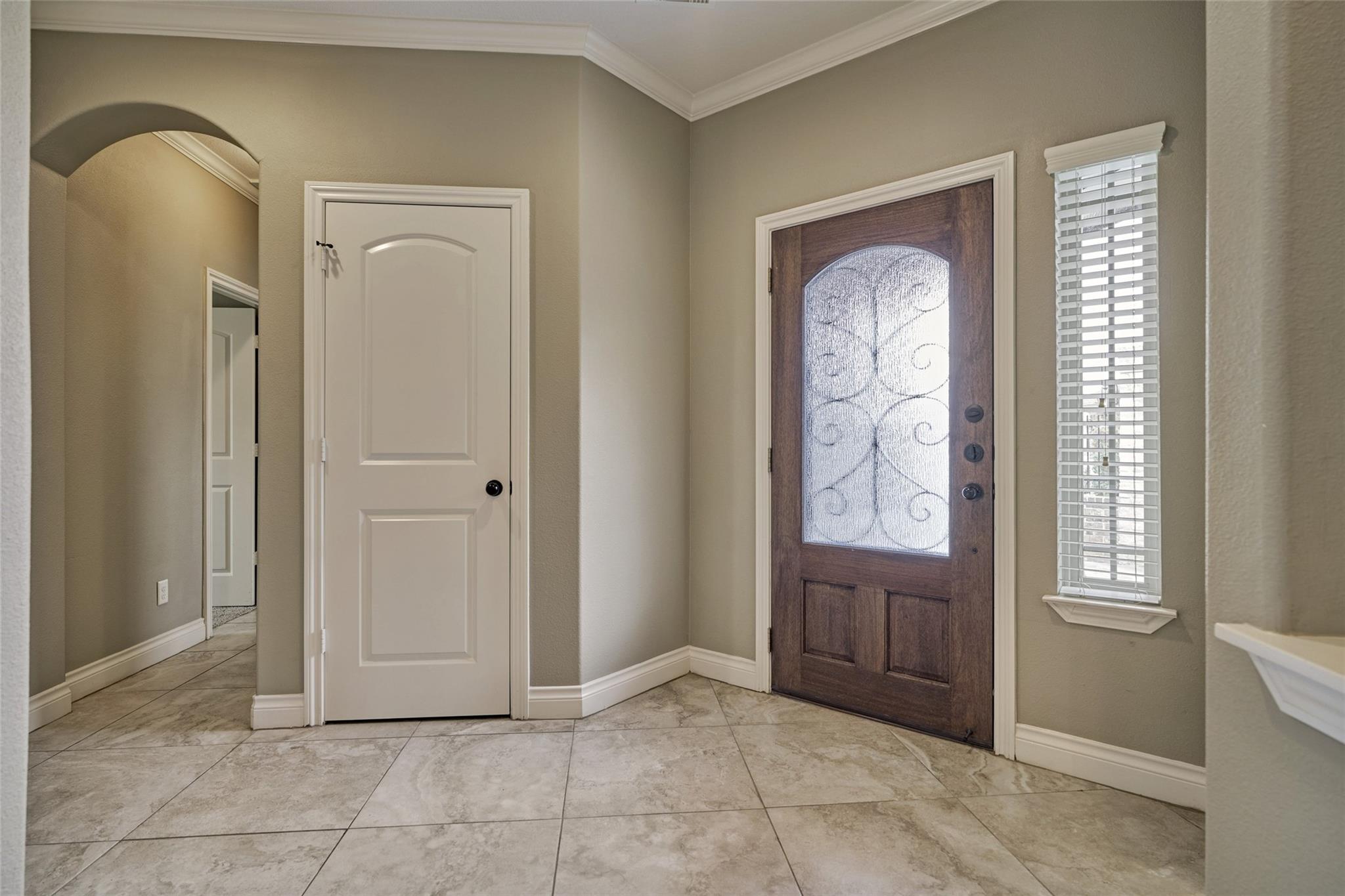 Entry foyer with a dark wood front door featuring decorative glass and large tiled flooring.